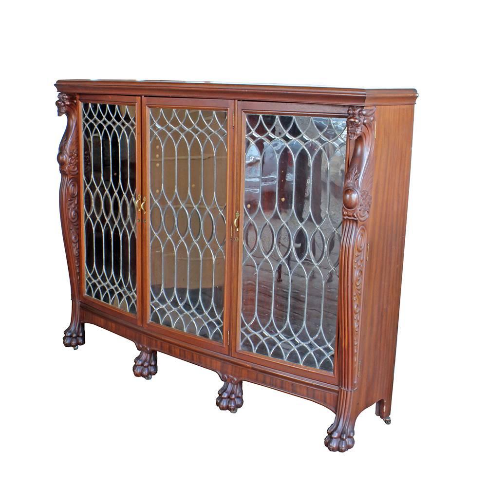 Beautiful craftsmanship in this incredible solid walnut bookcase. A gracefully curved front has three latching and locking doors, fronted with beautiful serpentined patterned leaded glass panels. Two snarling faced dragons stand as sentinels at the