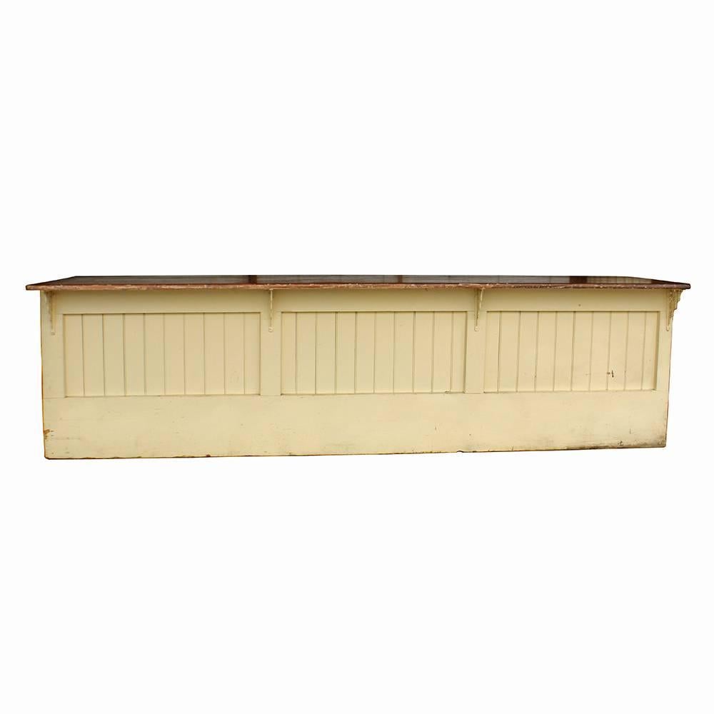 A pale buttercream yellow base fitted with bead board panels supports a richly stained wood top with a beautiful patina of its own. Graceful decorative iron brackets buttress the top and three generously sized storage cubbies provide plenty of space
