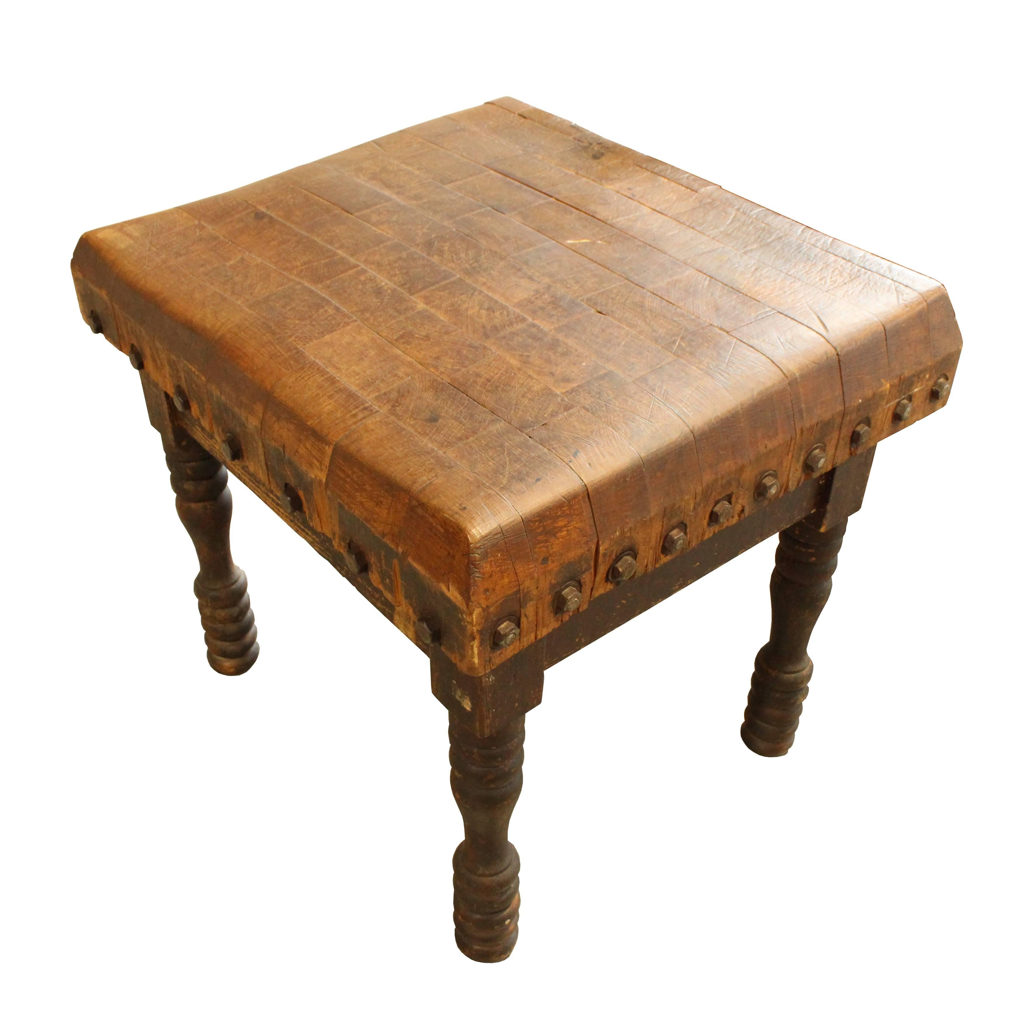 This early 20th century butcher block table features a beautifully worn top, which is accented by its exposed steel through bolts. This block also has very unusual spool type turning on its legs, giving striking visual appeal.