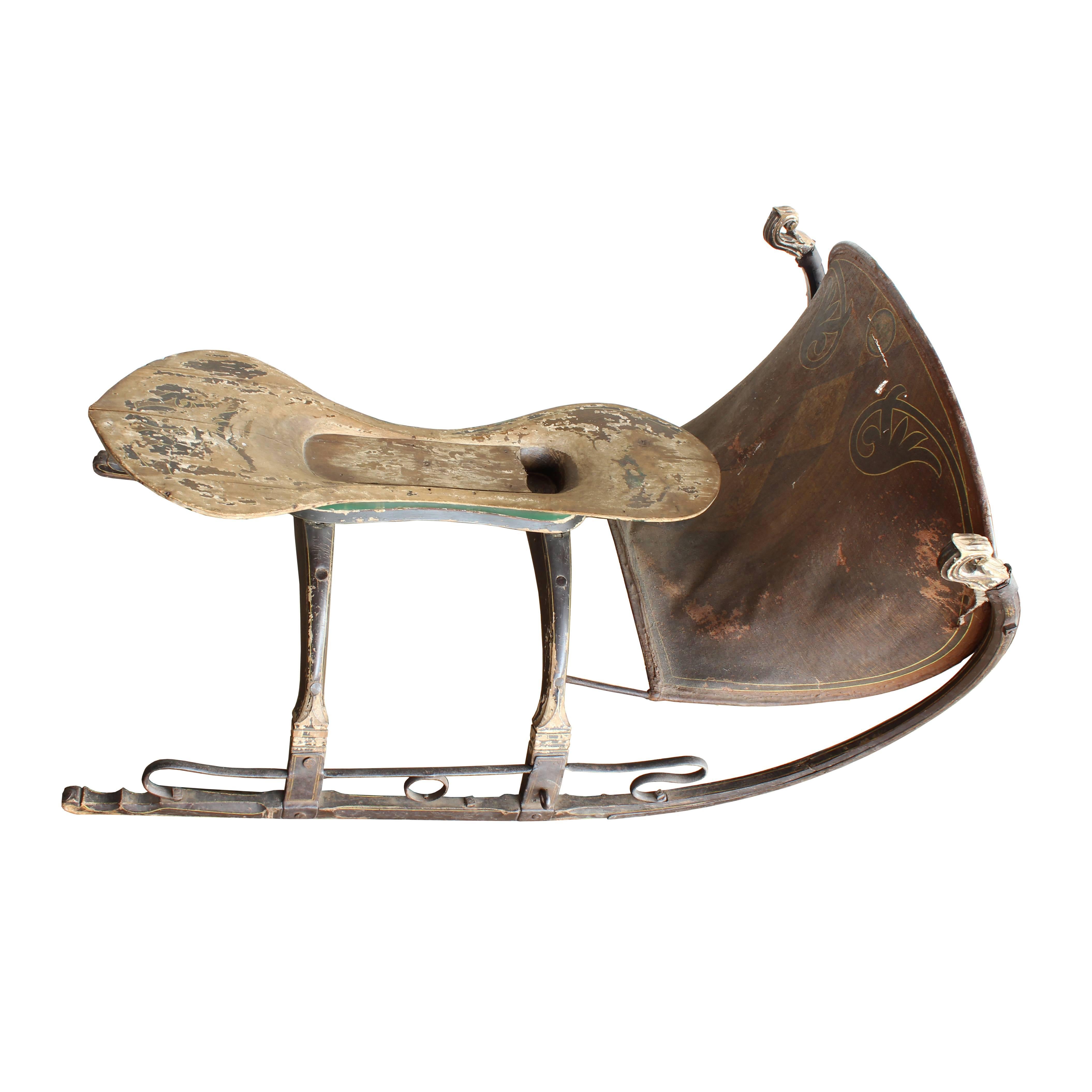The elegant design of this unusual small sleigh features wooden rails with hand-carved accents, hand-wrought iron and a canvas shield with a painted faux bois inlay design. The sleigh may have been built for racing.