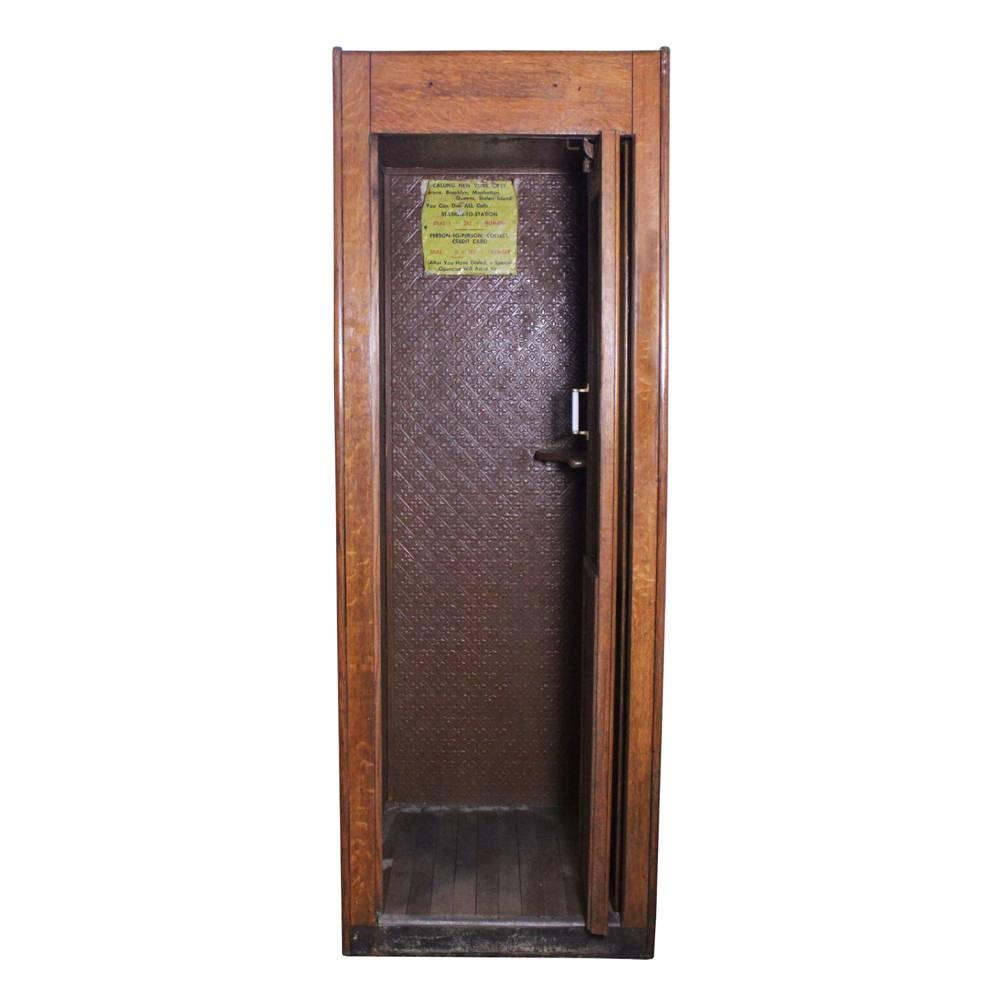 This oak telephone booth has a two-paneled glass door, small shelf for note taking, and a directional sign for making calls within New York its likely original resting place. The interior of the telephone booth is lined with patterned pressed tin.