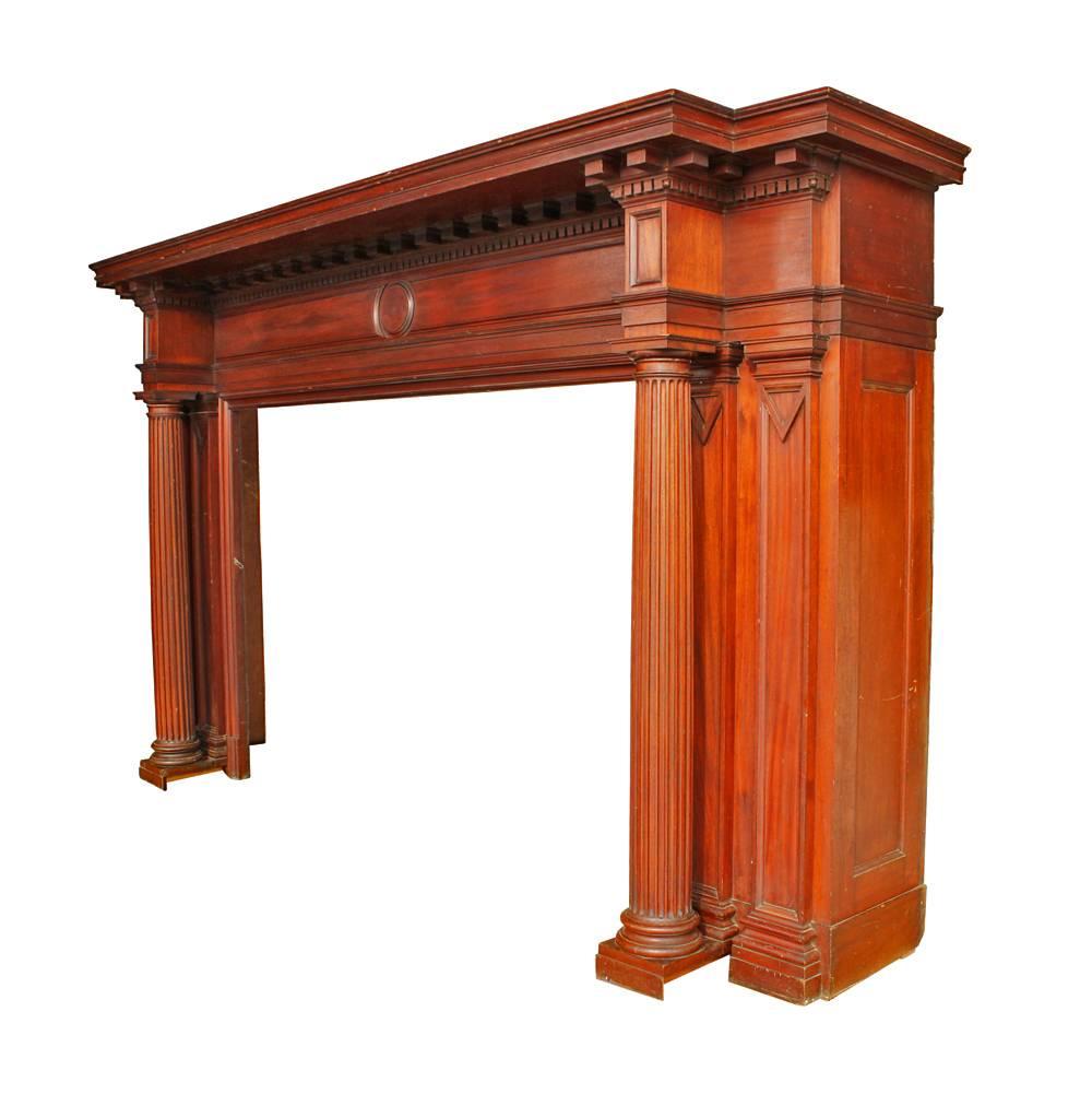 This striking mahogany mantel showcases the best in wood craftsmanship with its restrained use of classical elements. Highlights include a dentilled cornice, sharply defined edges, and a pair of fluted columns; this mantel is a handsome statement
