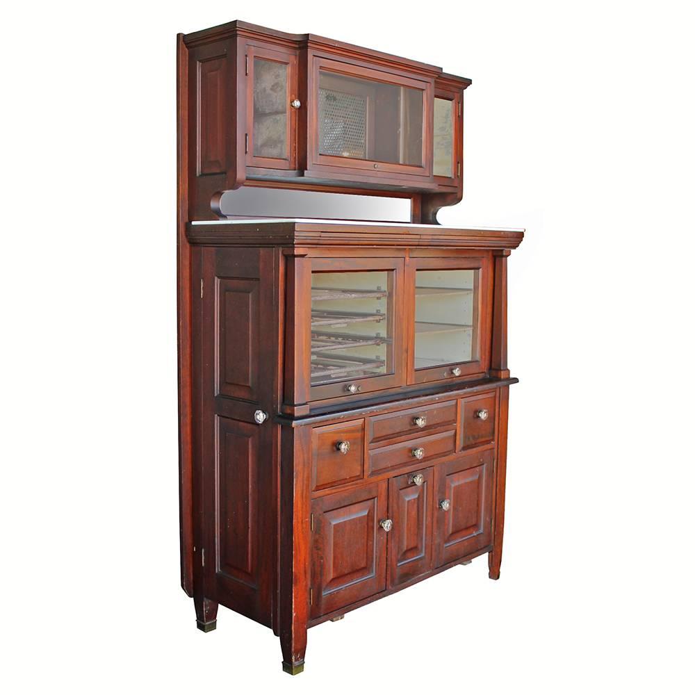 Manufactured in the early 20th century by the American Cabinet Company, this mahogany dental cabinet retains all of its original crystal hardware, including the key for the upper sterilizer cabinet. Made of solid mahogany with a milk glass shelf and
