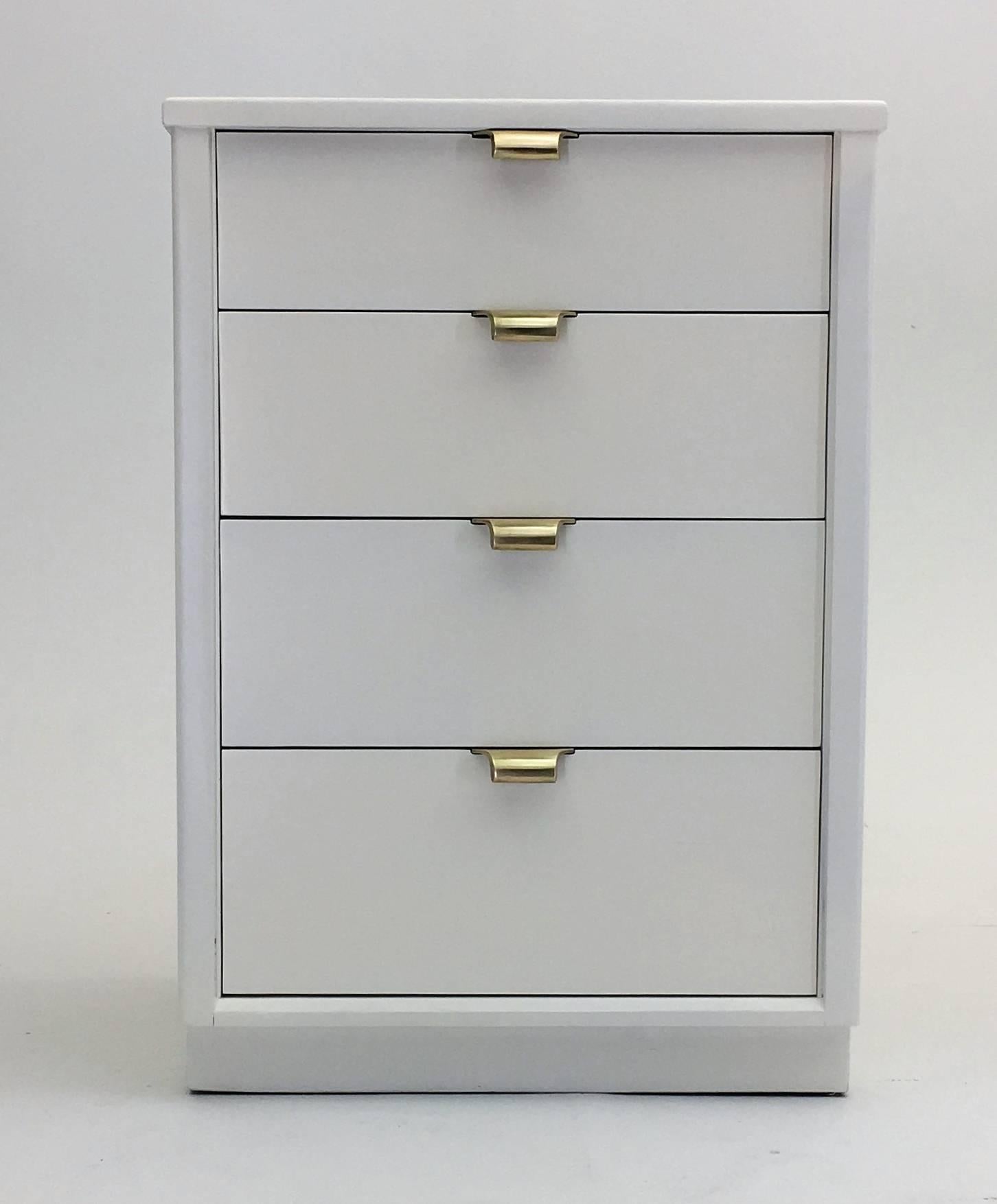 A beautiful pair of nightstands designed by Edward Wormley and executed by Drexel. This is one of the few designs performed outside of Dunbar and the linen white lacquer imparts a hollywood regency feel with the bold cast brass handles on each of