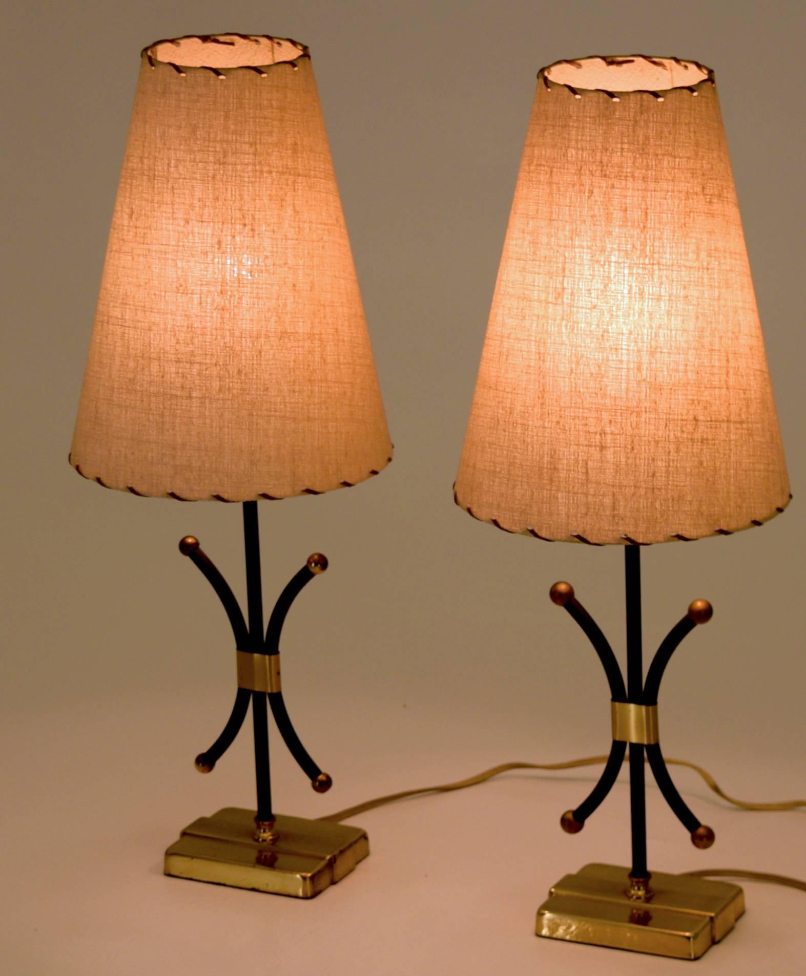 Fleur-De-Lis motif 
Likely Produced in France
circa 1950
Eight round and 22 inches tall.

A fine pair of minimalist boudoir style petite lamps with linen shades with leather strapping. The lamps are produced with brass accents and knobs and bases