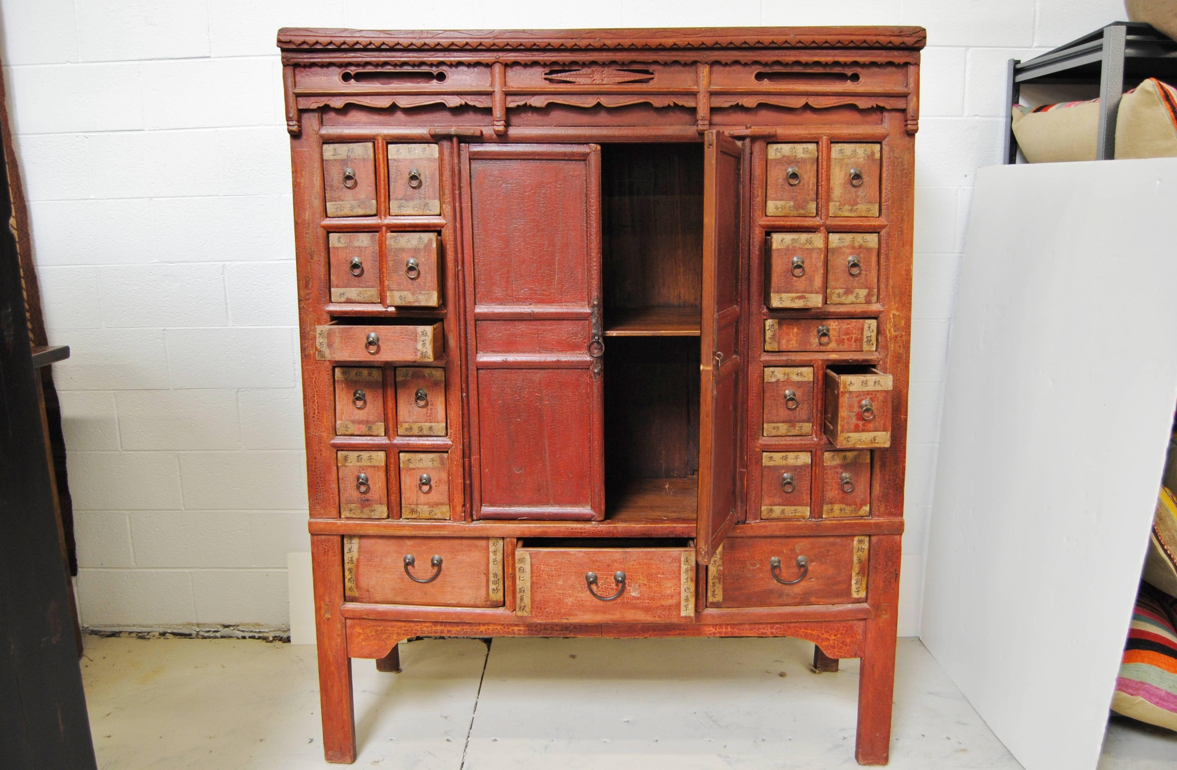 Antique Chinese elmwood apothecary armoire with 21 drawers and a pair of center doors that open to a large storage area. The Asian armoire has beautiful hand-carved detail typical of the older Shanxi cabinets. All original lacquer and paint.