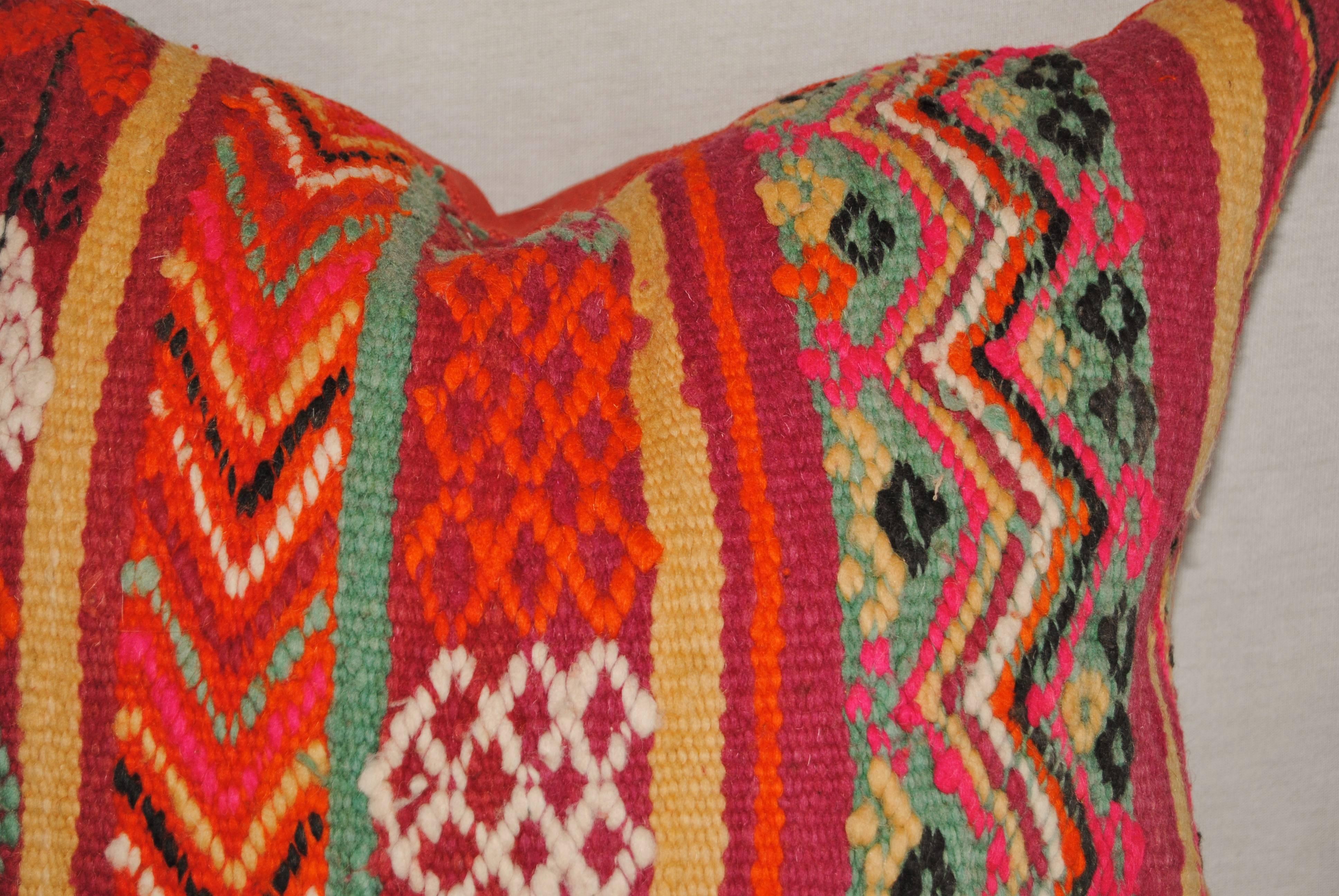 Custom pillow cut from a vintage hand loomed wool Moroccan Berber rug from the Atlas Mountains. Soft lustrous wool with wonderful tribal designs in vivid colors. Pillow is backed in an orange/red linen, filled with an insert of 50/50 down and