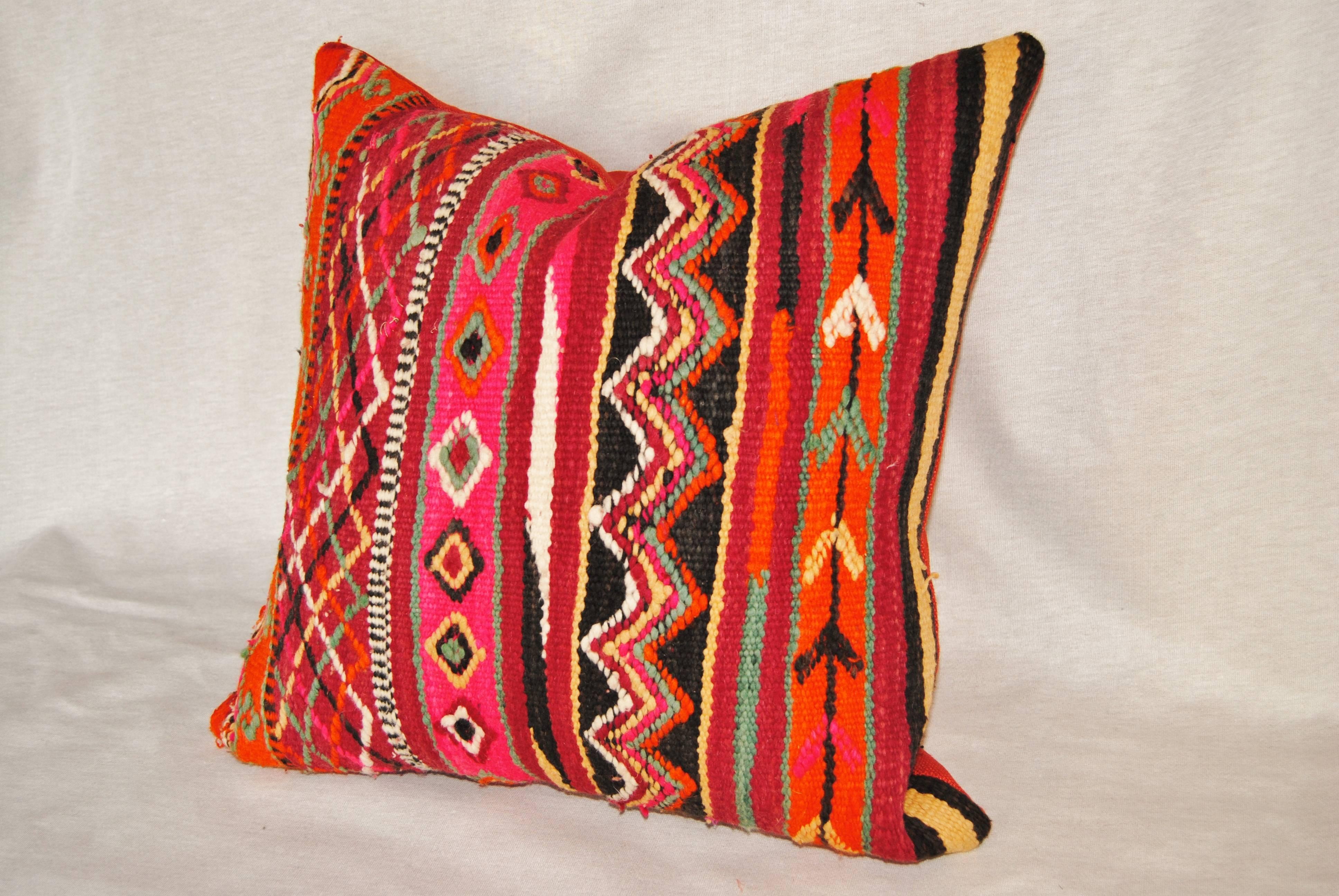 Custom pillow cut from a vintage hand loomed wool Moroccan Berber rug from the Atlas Mountains. Wool is soft and lustrous with vivid colored tribal designs. Pillow is backed in an orange/red linen, filled with an insert of 50/50 down and feathers