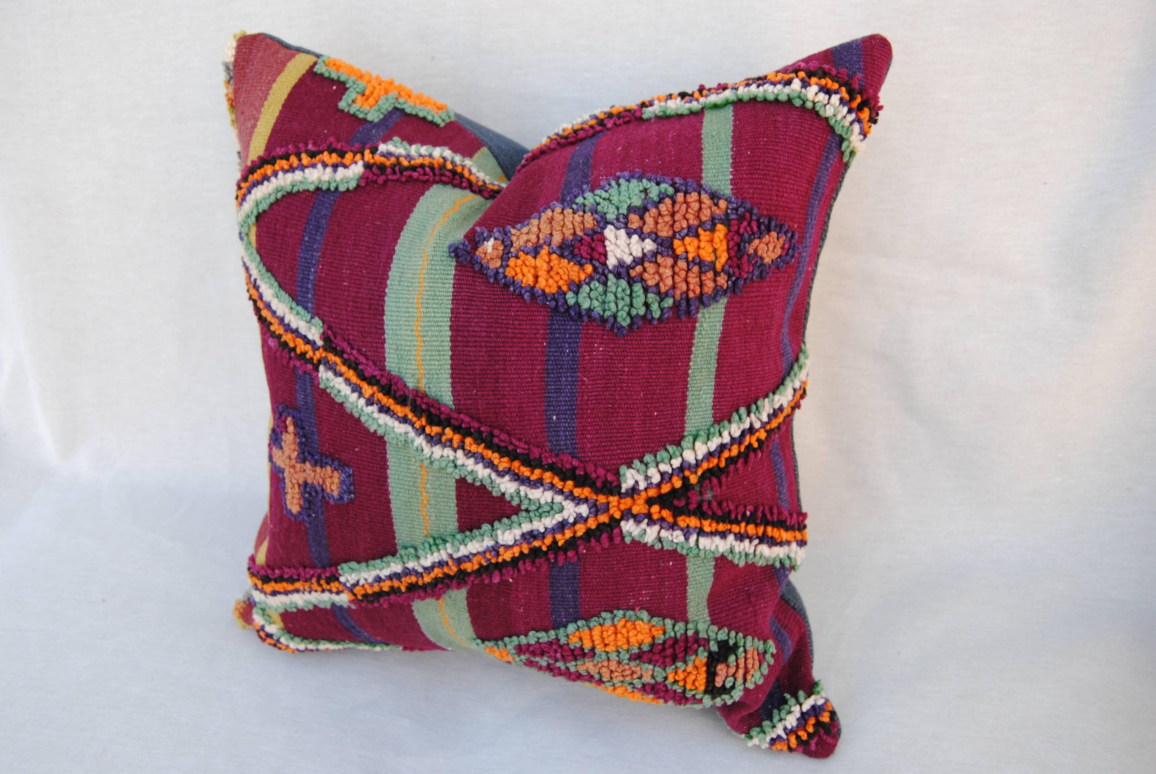 Custom pillow cut from a hand-loomed wool Moroccan Berber rug from the Atlas Mountains. Wool is soft with strong natural colors. Flat-weave stripes are embellished with tufted wool tribal designs. Pillow is backed in a dark blue linen blend, filled