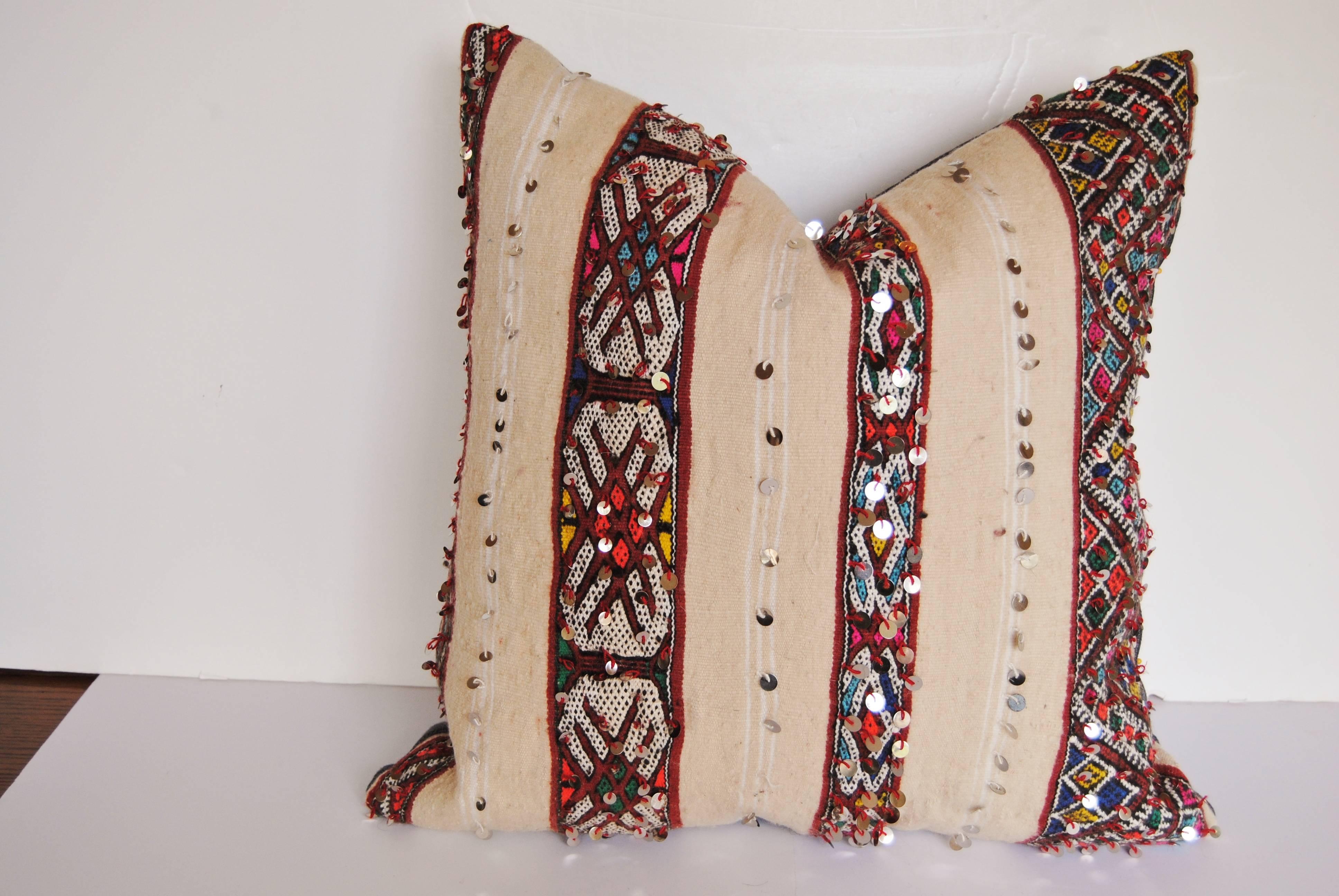 Custom air of pillows cut from a hand-loomed wool Moroccan rug made by the Berber women of the Atlas Mountains. Brightly colored bands are embellished with sequins against a creamy wool textile. Pillows are backed in a deep purple linen, filled with