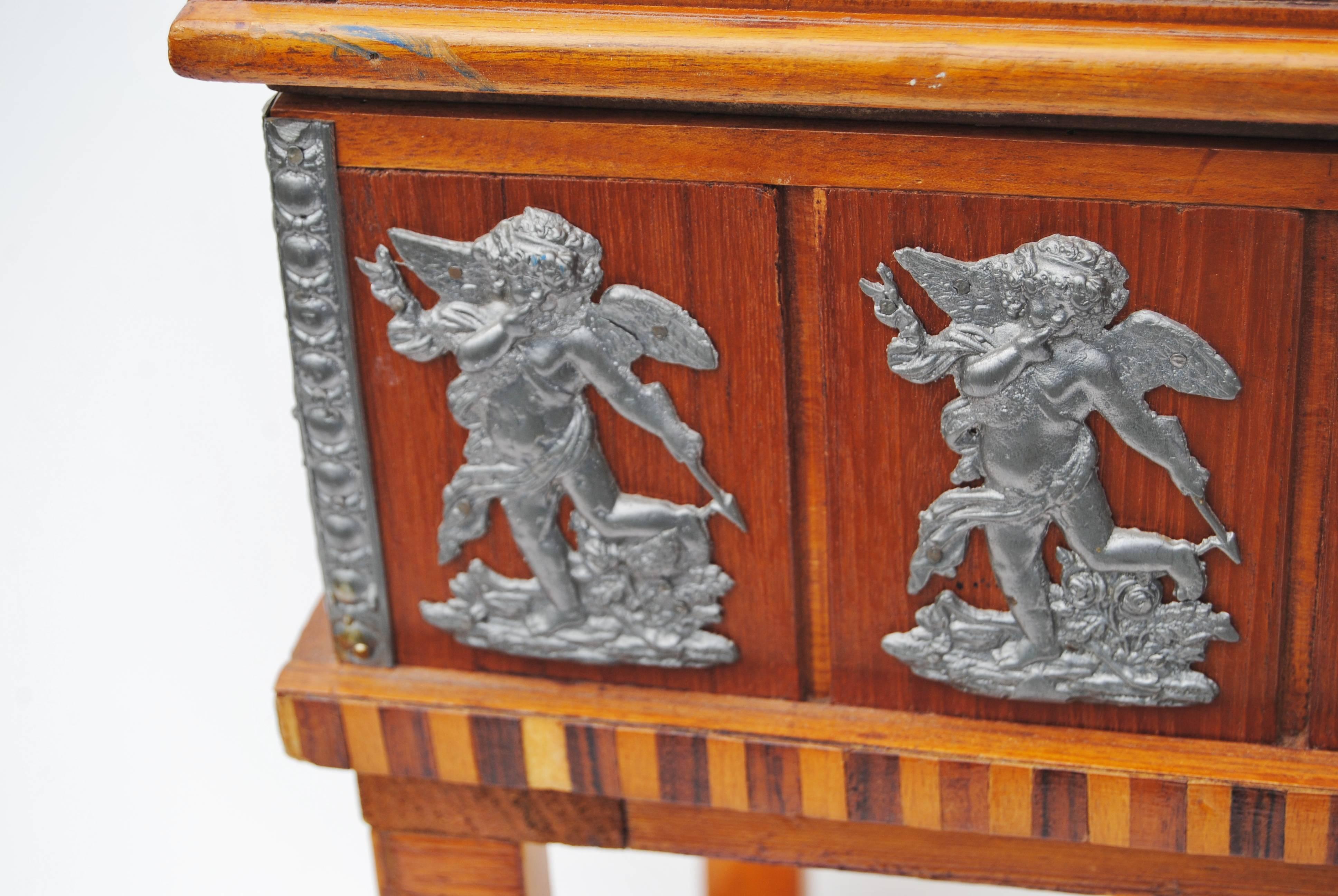 Vintage Danish handcrafted Folk Art cabinet. It has decorative applied pewter or similar metal with angels and scrolling. Veneer work covers the case of the cabinet with a lift up lid and removable partitioned tray. Legs are typical of Scandinavian