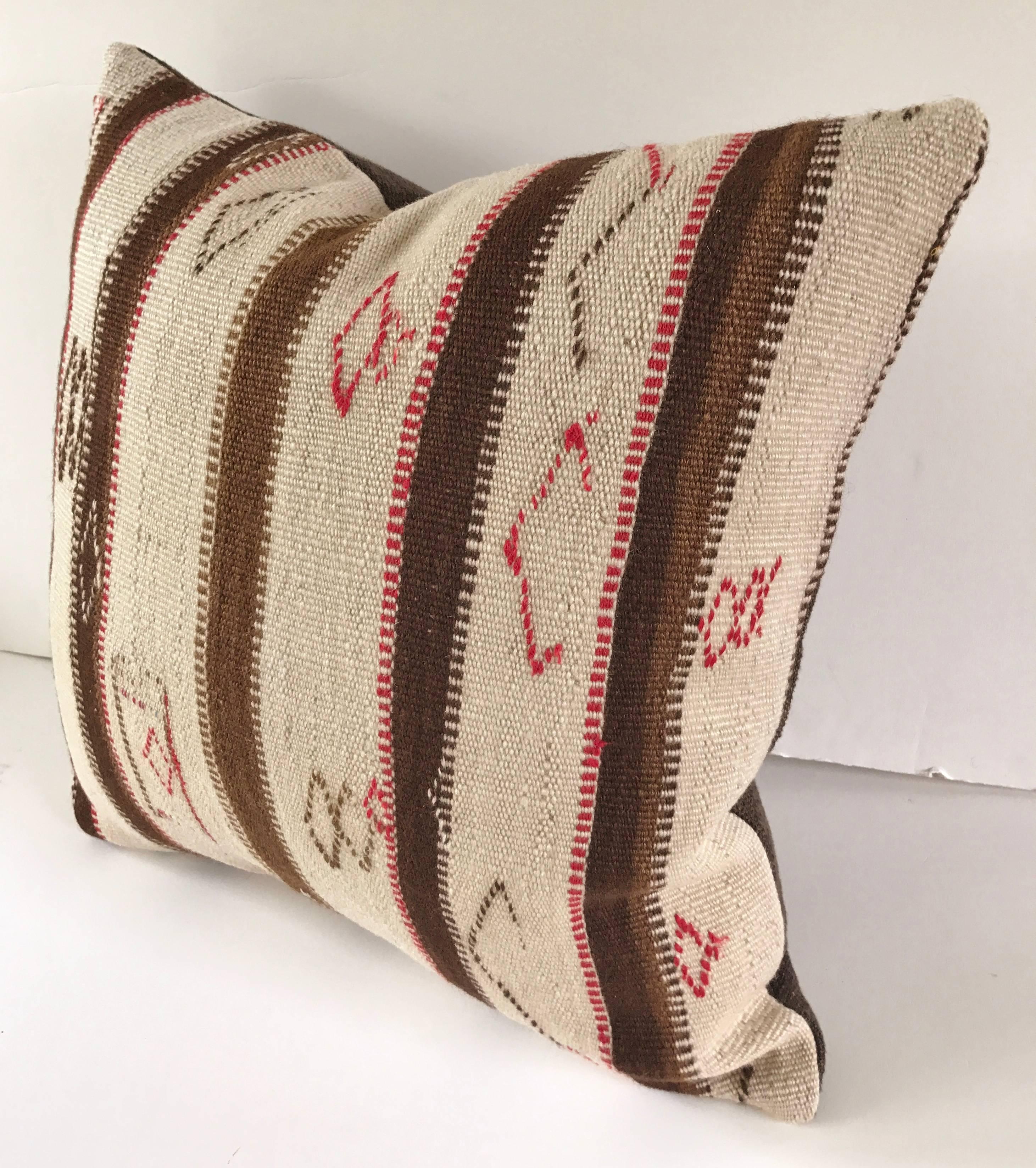 Custom pillow cut from a vintage hand loomed wool Moroccan Berber rug from the Atlas Mountains. Wool is soft and lustrous with tribal designs incorporated into the stripes. Pillow is backed in a dark brown linen blend, filled with an insert of 50/50