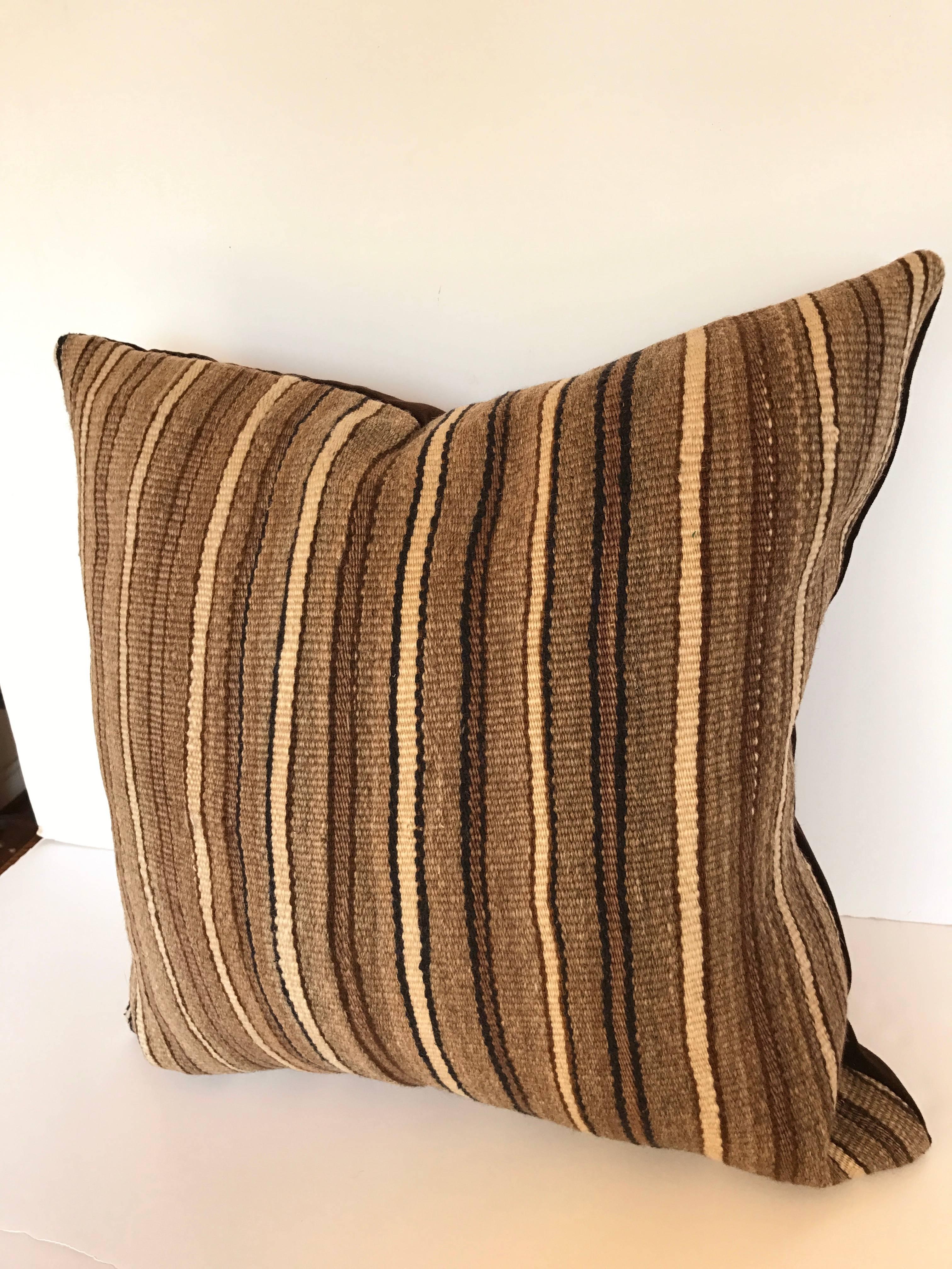 Custom pillow cut from a vintage hand-loomed wool Moroccan Berber rug from the Atlas Mountains. Woo is soft and lustrous with all natural dyes in browns, cream and navy stripes. Pillow is backed in dark brown velvet, filled with an insert of 50/50