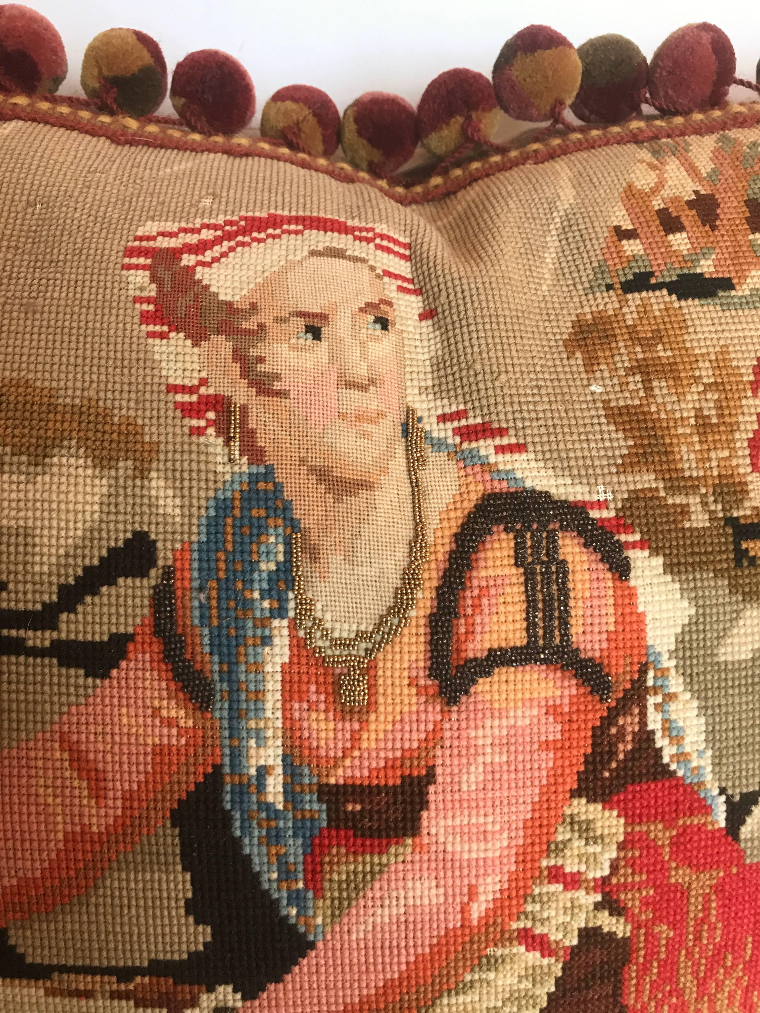 Custom one of a kind pillow cut from an antique English needlepoint tapestry. Very fine work on the detail of the faces with metallic beading. Minor loss of wool in background area due to age of piece. Tapestry is trimmed with designer wool ball