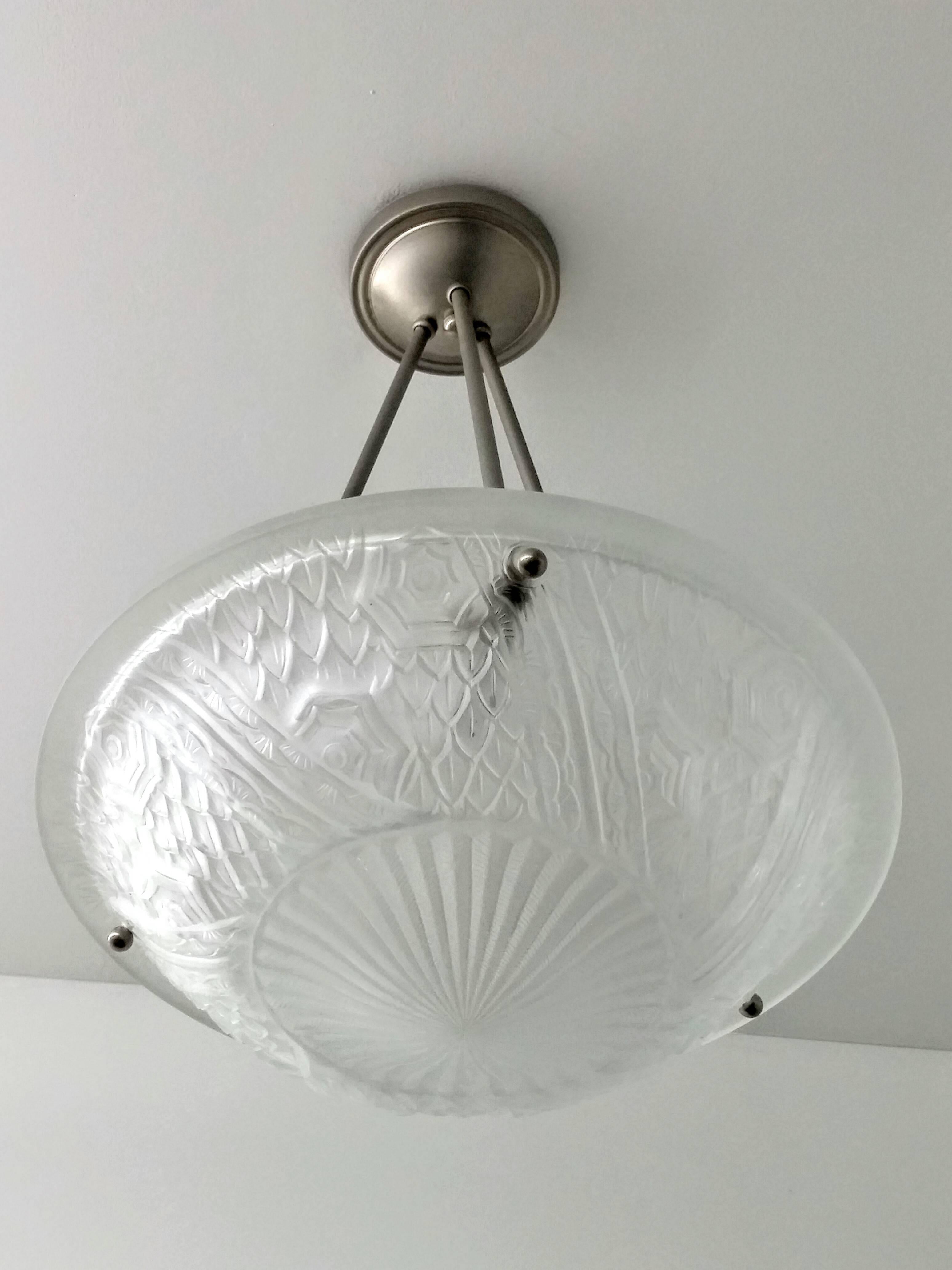 A French Art Deco pendant chandelier by the French artist “Schneider“ in great condition. Clear frosted molded glass shades with intricate flowers and geometric polished motif details held by three smooth rods with a matching canopy. The fixture has