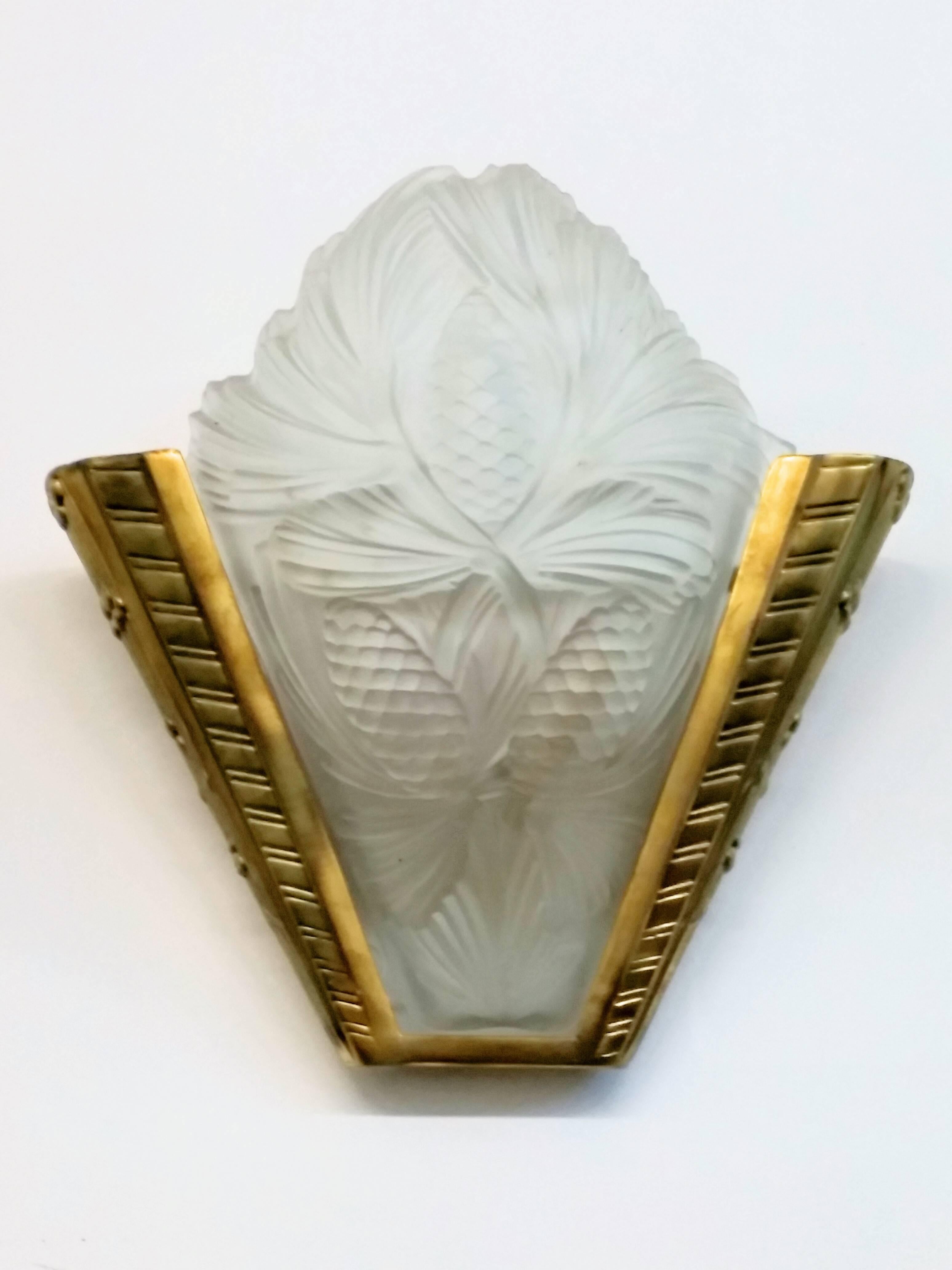 Ein Paar französischer Art-Deco-Wandleuchter aus geformtem Milchglas mit Tannenzapfenmotiv und polierten Details in gutem Zustand. Sie ruhen in Bronzerahmen mit geometrischen Motiven. Die Wandleuchten wurden für die US-Normen umverdrahtet. Jede