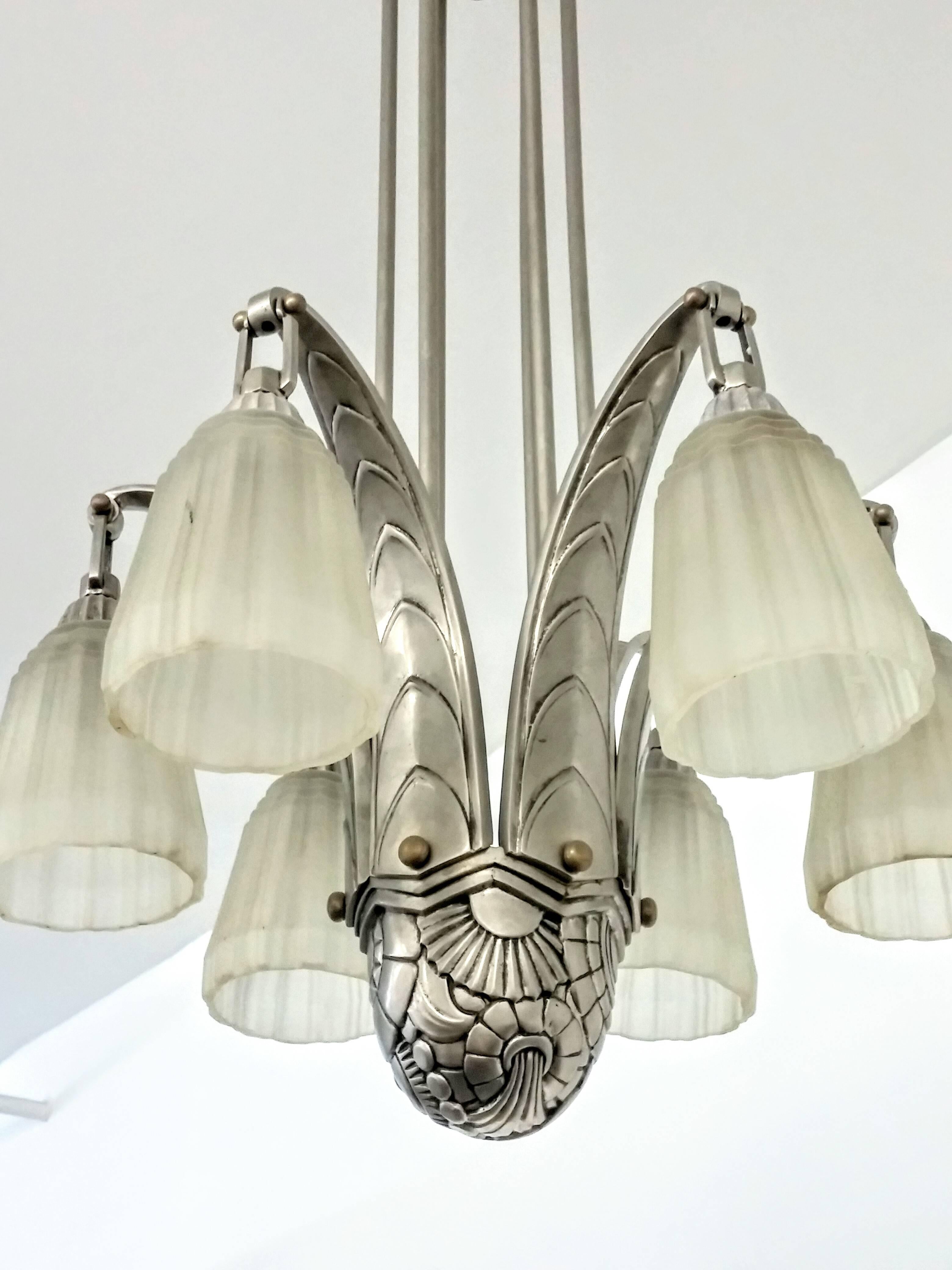 
A stunning French Art Deco chandelier with a half dome flower geometric motif centerpiece supporting six stylized overlapping leaf design arms, issuing conical frosted glass ribbed tulip designs. Six rods are held by a matching cone shaped canopy.