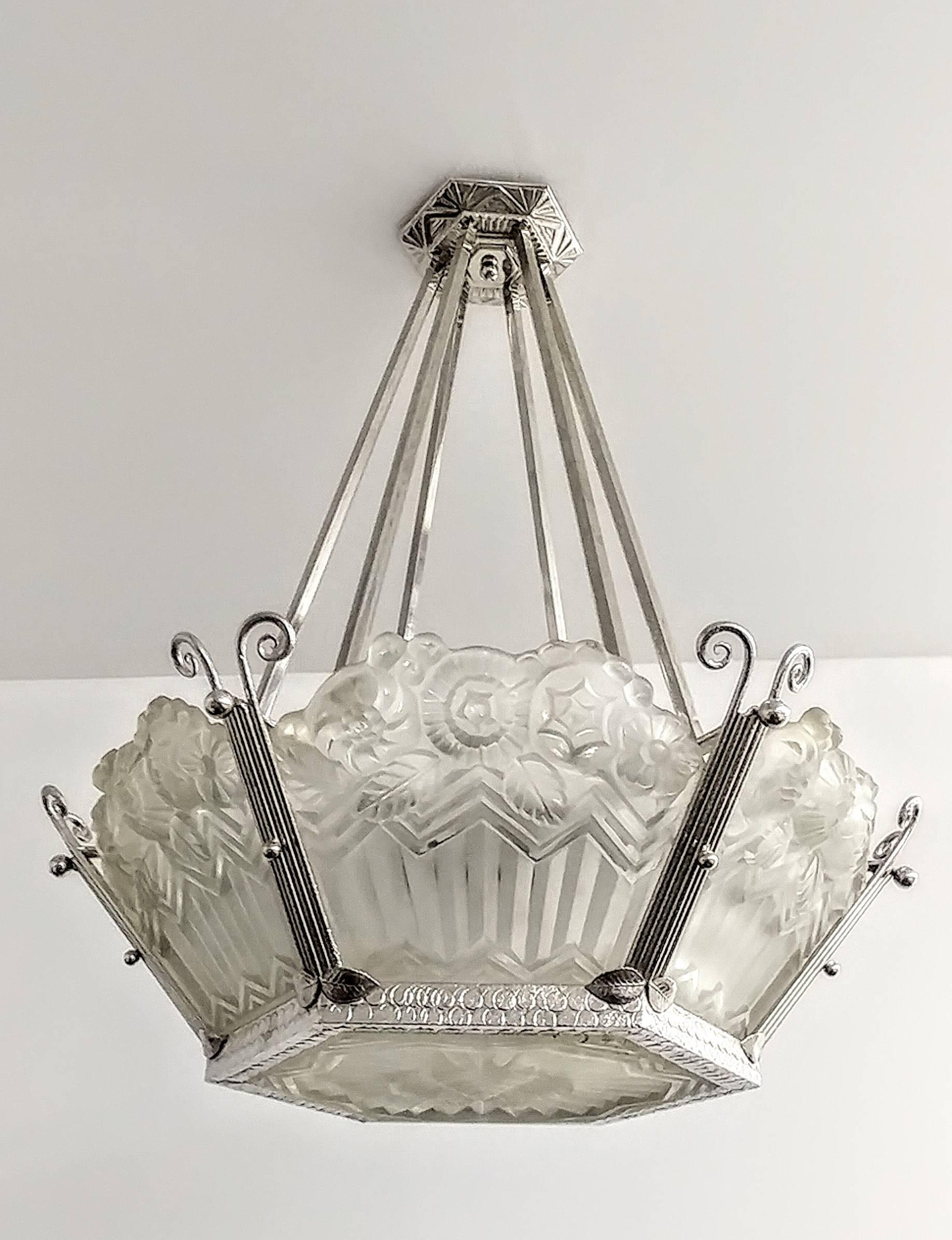 A French Art Deco chandelier by Jean Noverdy. Six shades with matching center coupe in clear frosted glass with intricate flowers with geometric motif details. Each shade marked Noverdy France. Supported by a nickeled wrought iron frame. Chandelier