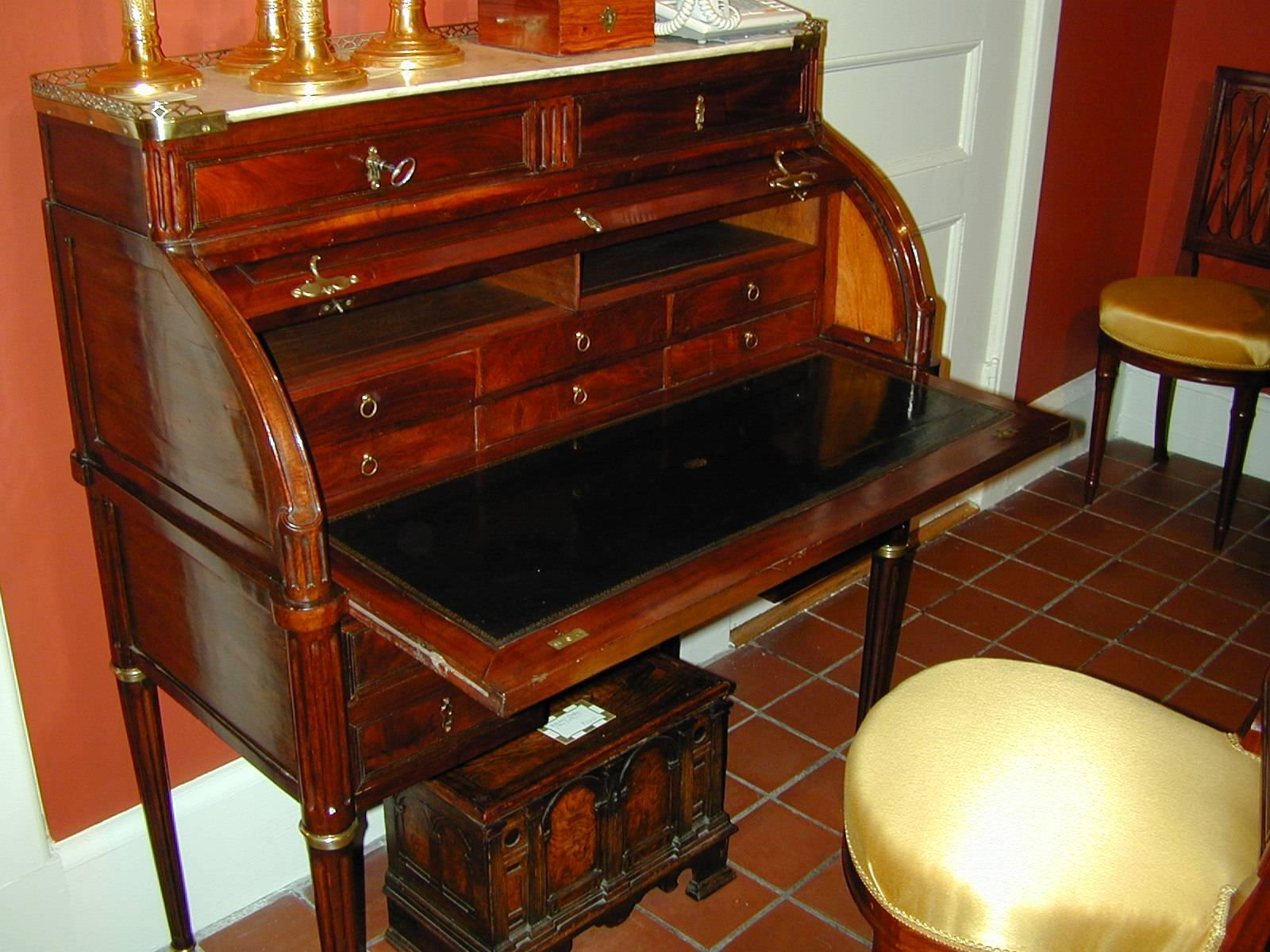 The desk with a 1/4 cylinder top that opens to reveal a leather writing surface with pigeon holes and drawers. The gallery with white Carrara marble top.