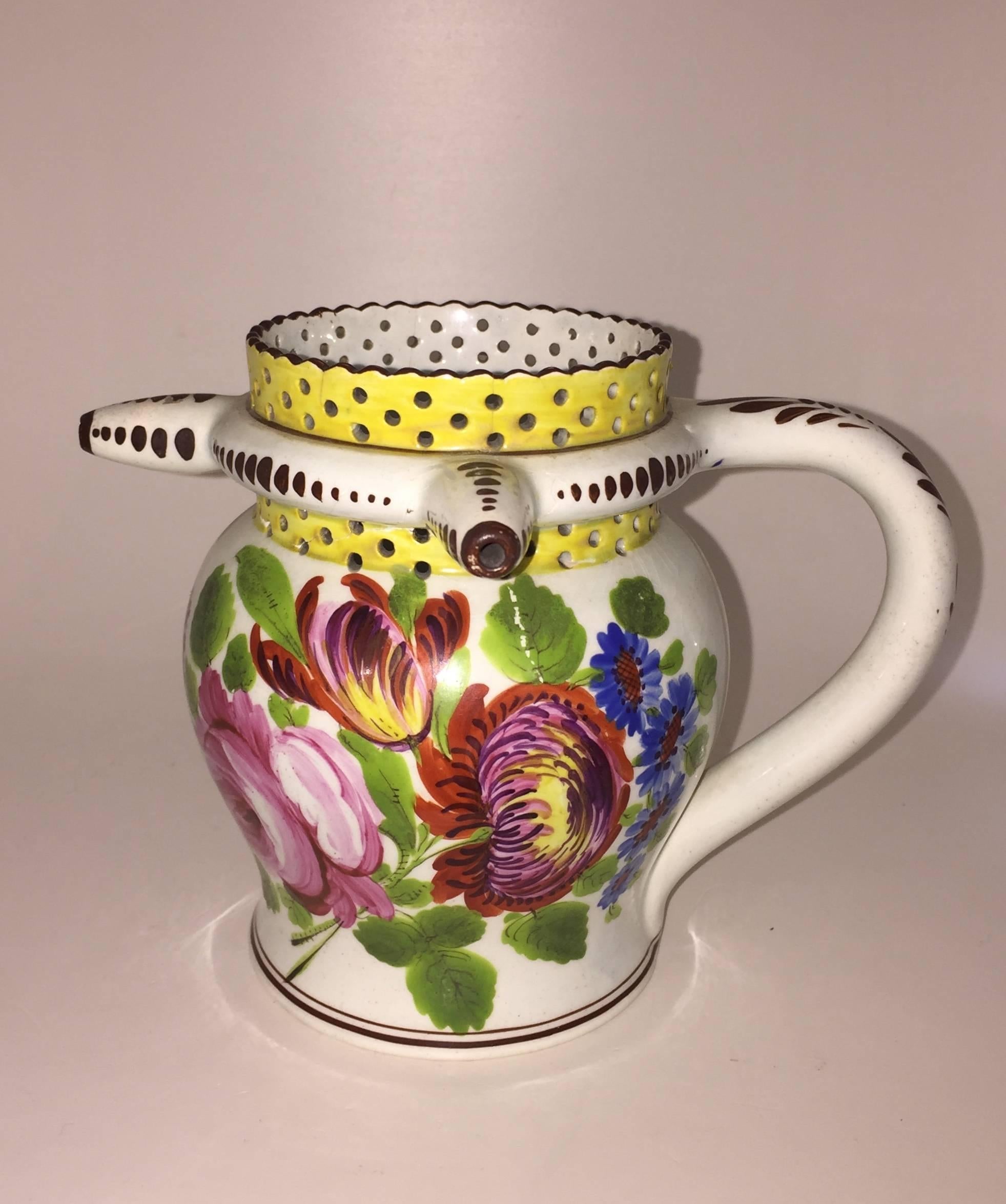 The puzzle jug consisting of a handle with pierced yellow painted decoration above and below the band of three spouts, floral painting on each side with intials 'JA' and date '1823' within a wreath in the centre. The jug has been reglued with cracks