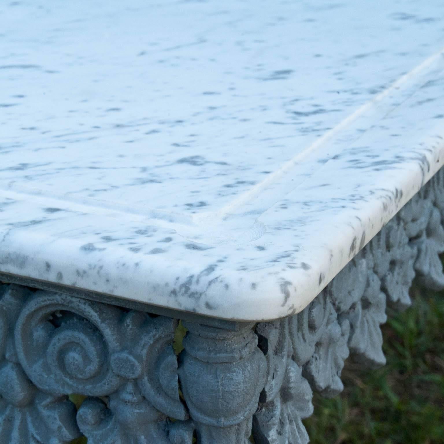This very decorated console table has been made of a wrought iron base and a cast iron ornate frame, which is topped with an elegant white Carrara marble top with rounded edges. This “Fin De Siecle” butcher table is still seen throughout France, due