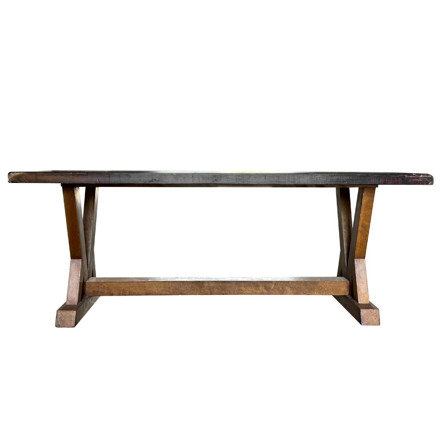 A substantial French trestle table crafted circa 1940, featuring a striking black-stained walnut top with a rich, matte patina. The rustic yet elegant design is supported by a sturdy base in natural wood with angled supports and a central stretcher,