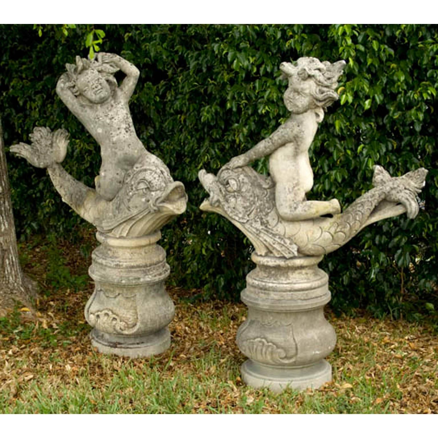 Exceptional pair of cherub statuettes, riding on dauphins grotesques and positioned onto circular detailed bases with centered scrolls. These garden ornaments were formerly used as water features.