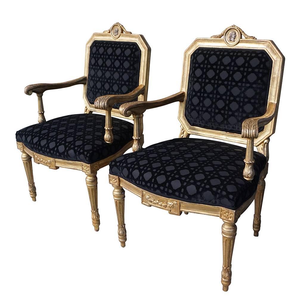 Late 18th Century, an antique pair of Italian gilded fauteuils with ornate armrests, the back rests are adorned with centered medallions, enhanced by detailed wood carvings, in good condition. The dining armchairs represent the Louis XVI period. The