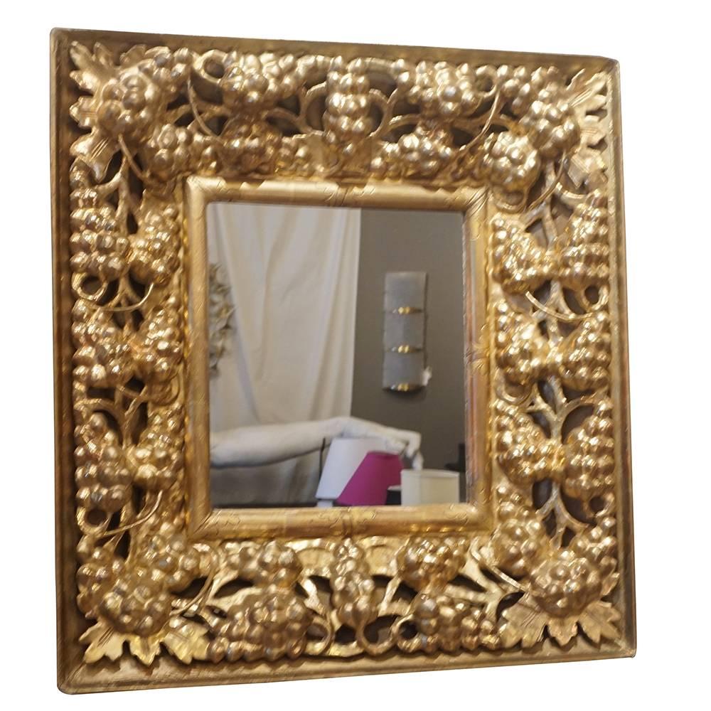 An antique, very richly Italian hand carved mirror with a gilded wooden frame, adorned with grapes and foliage and original mirror glass, in good condition. The small mirror represents the Baroque time period. Wear consistent with age and use, Circa
