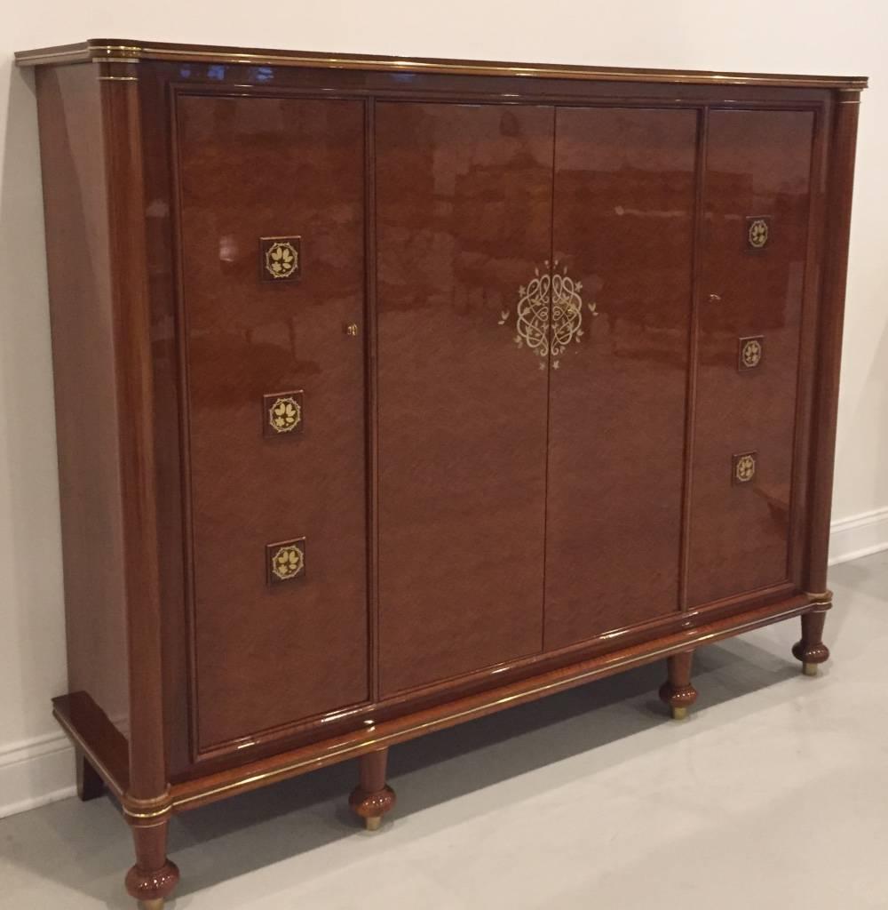 This sunning French Art Deco cabinet is designed by famous artisan Jules Leleu. The cabinet reflects the craftsmanship and quality of the Art Deco period. The bronze trim is pictured over four parquetry front doors with gold hardware. It is a signed
