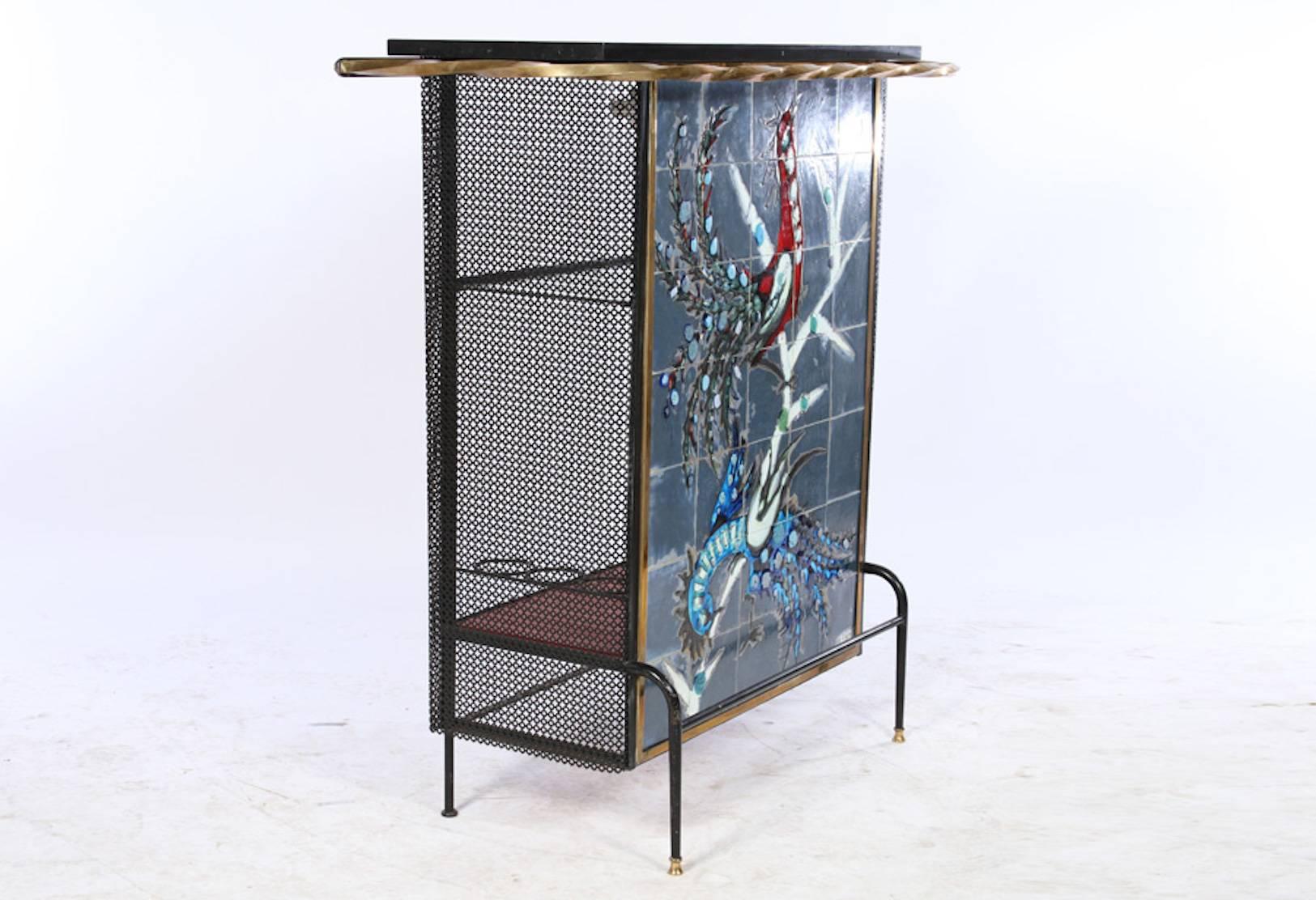 This tile front iron and bronze Mid-Century dry bar is fun and inviting, coming with two bar stools. The tile face depicting two peacocks is signed by 'Wilhelmy,' circa 1950. The stools are 32