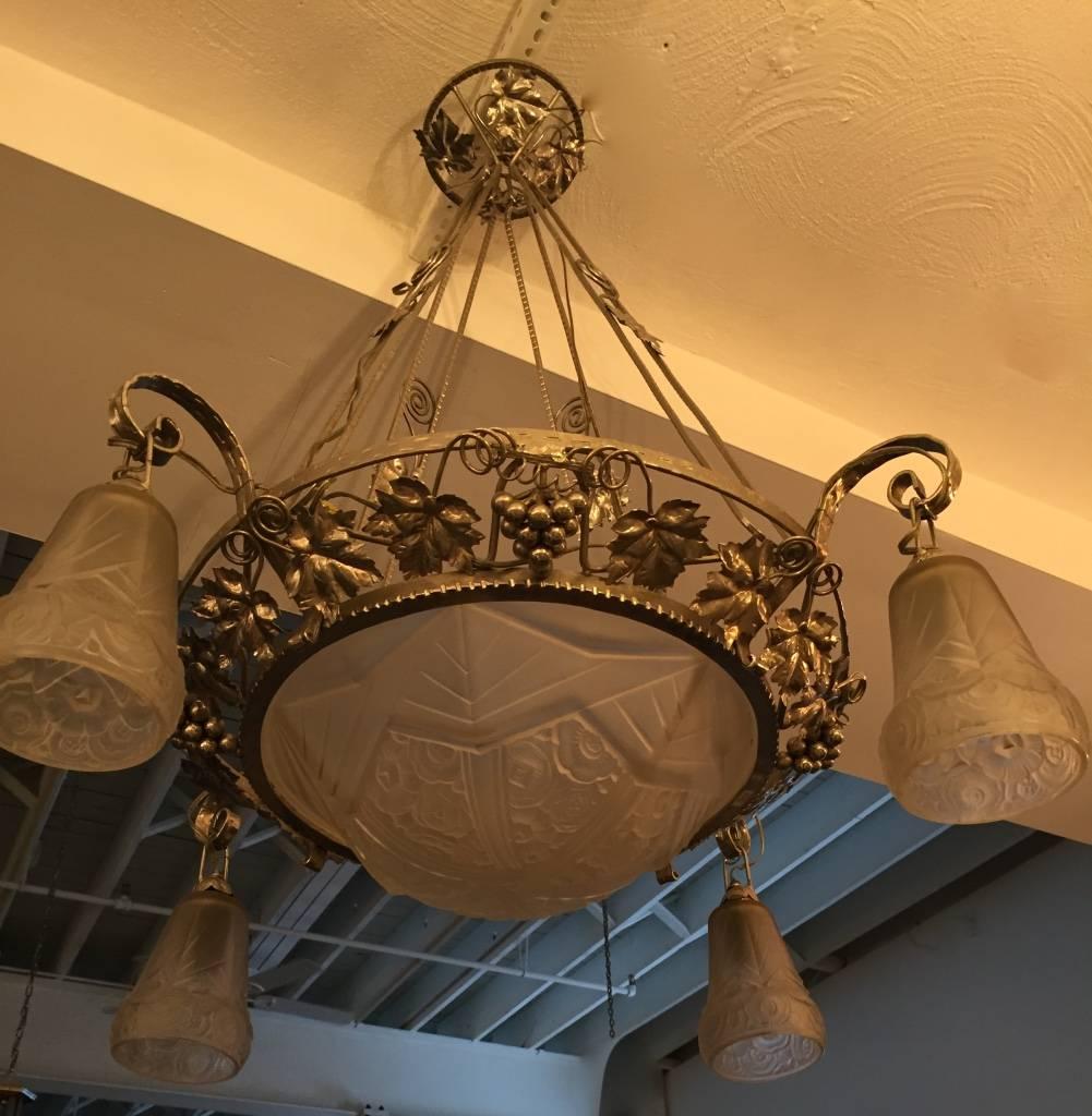 This French Art deco Chandelier has grapes and leafs motif surrounding the outer bowl on the metal work, with four tulips hanging on the side. With leaves on the ceiling plate. The glass has geometric patterns with flower intertwined, giving a