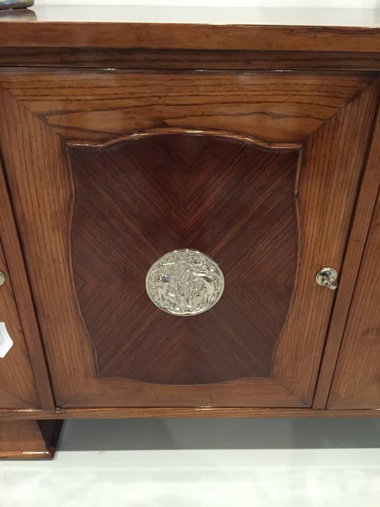 This spectacular five door French Art Deco credenza has silver plaques on each door with a deer motif. The center door opens to reveal draws inside. While the other doors reveal shelfs for plenty of storage. The two tone buffet is very elegant and