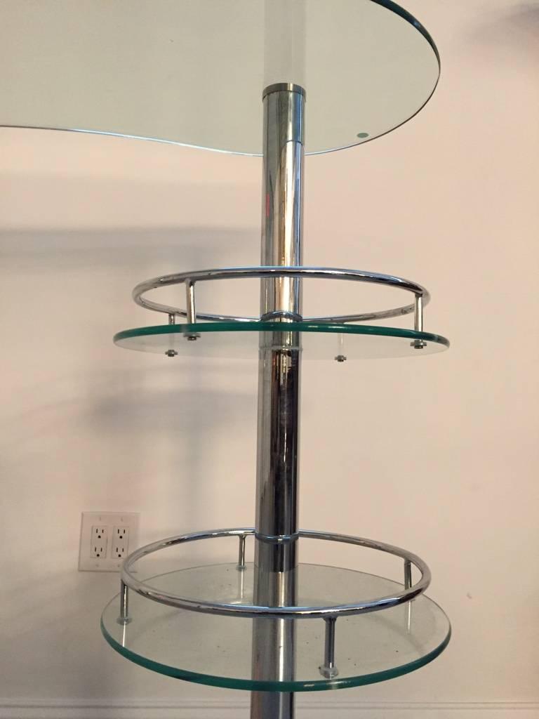 Mid Century Modern chrome and glass dry bar. Having three-tiers for bottles and glassware. Along with a curved glass top. 
