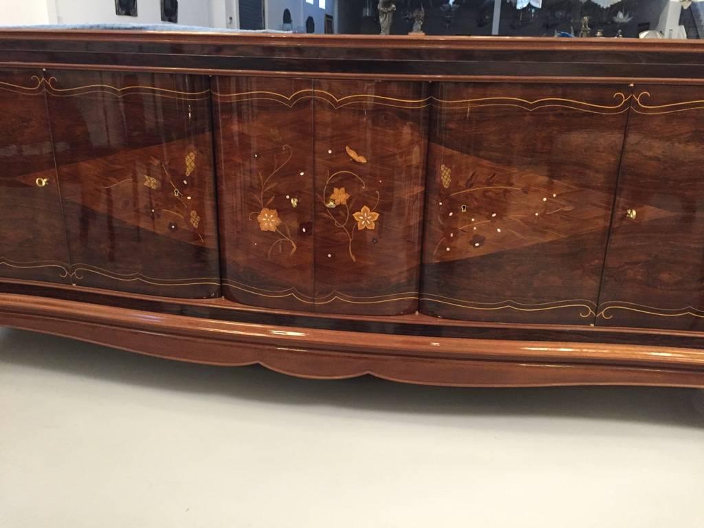 Gorgeous French Art Deco six-door buffet in the style of Jules Leleu. With beautiful Rosewood and mother-of-pearl inlay along with stunning marquetry. The middle doors open to reveal a bank of draws while the outer door reveal shelfs. Having