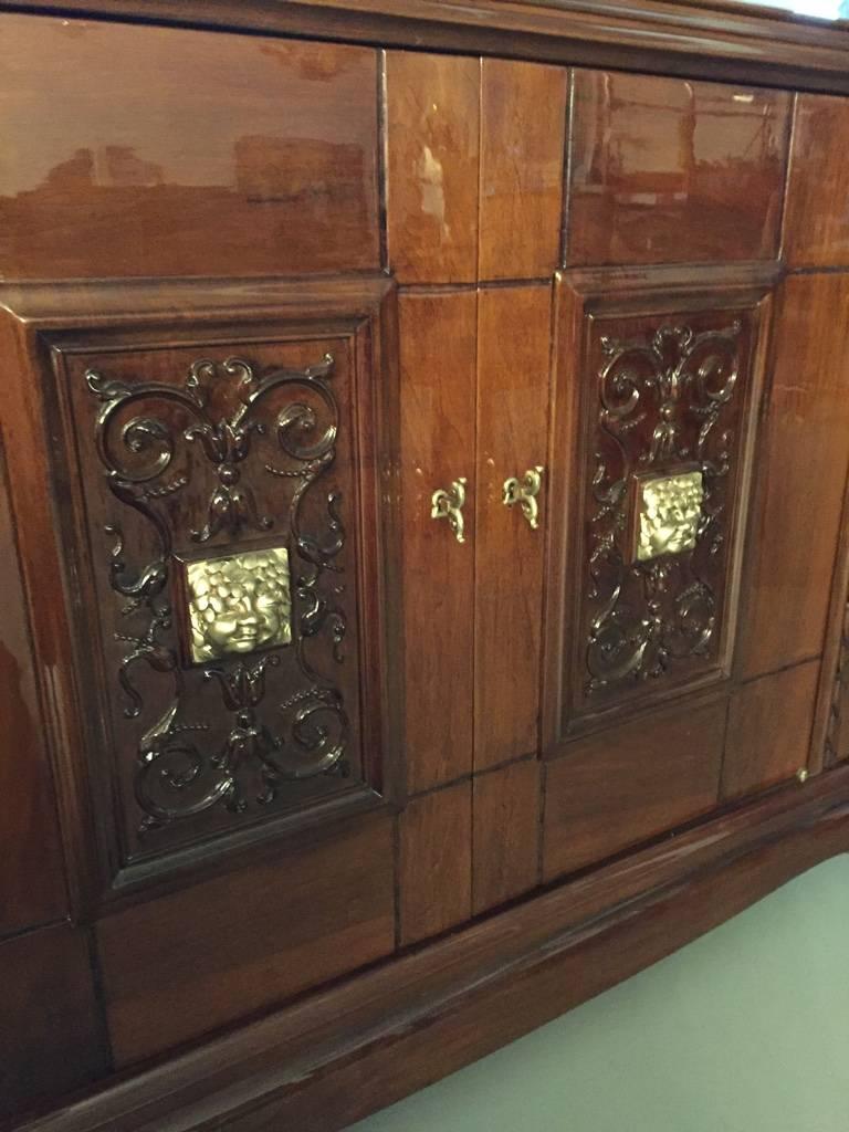 Stunning French Art Deco walnut credenza with bronze face in the front doors. This sideboard has been professionally restored having a very high French polish. The two center doors have a floral bronze face with beautiful deco details. Inside one of