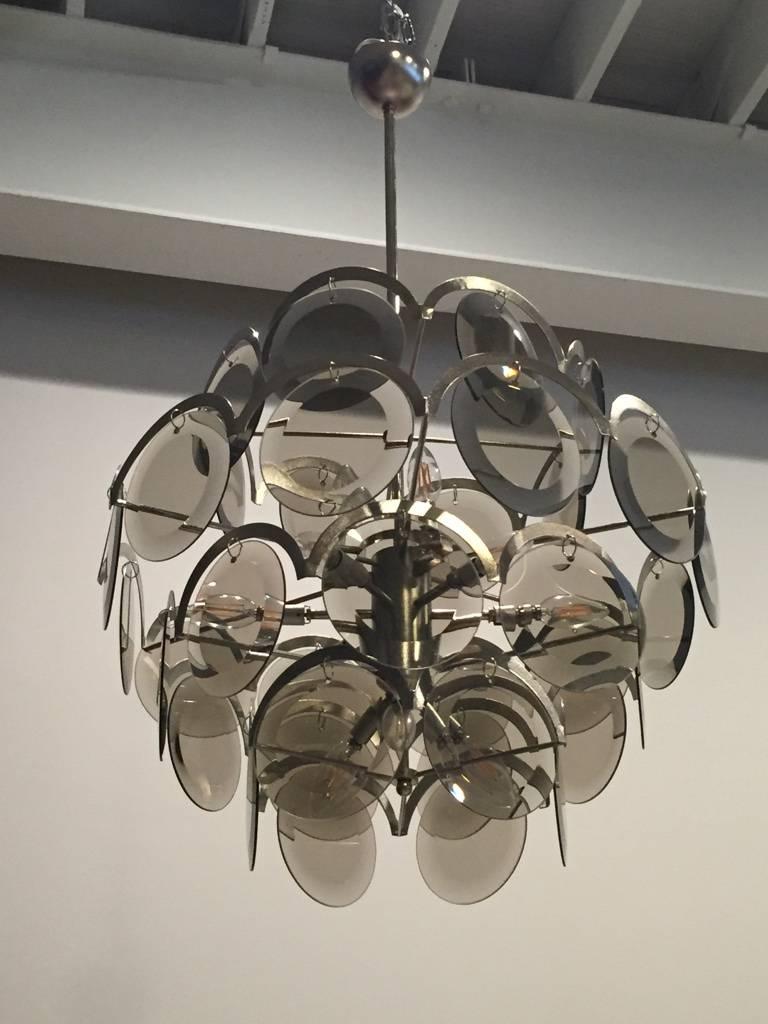 Magnifique lustre italien moderne du milieu du siècle par Vistosi Murano. Ayant quatre niveaux de disques en verre Murano gris fumé. Suspendu à un cadre chromé. 

   