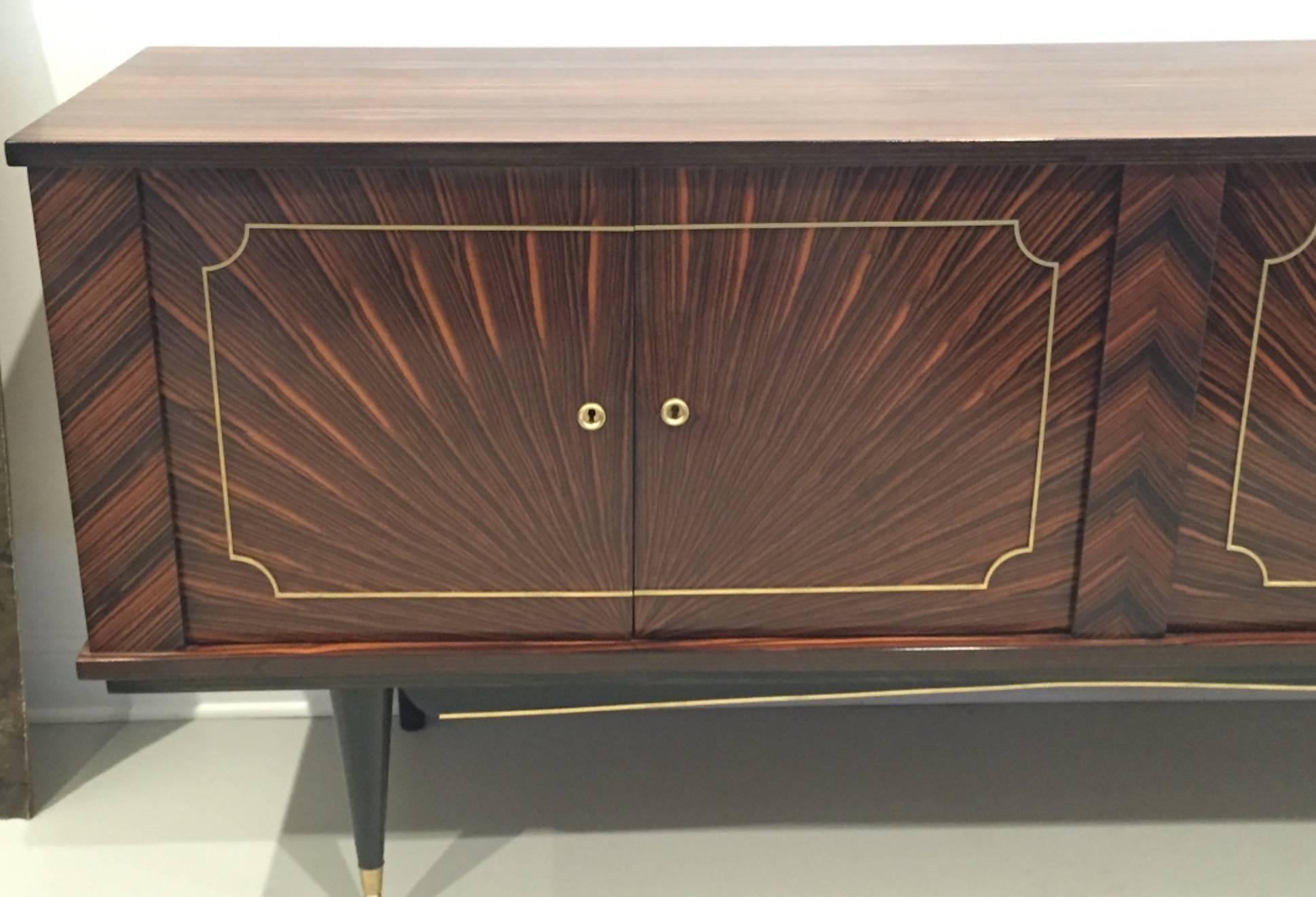 This spectacular French Art Deco Macassar "Starburst" buffet is stunning. Doors open to reveal dry bar and plenty of storage. The brass hardware accents the buffet beautiful and is very elegant. Having beautiful ebony legs. Has been