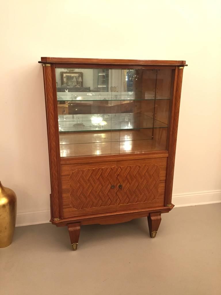 This French Art Deco Palissandre (rosewood) vitrine by Jules Leleu (1883–1961) is from the 1930s and features a top compartment with two sliding glass doors and a glass shelf. A lower compartment has two wood doors with inlay marquetry and bronze