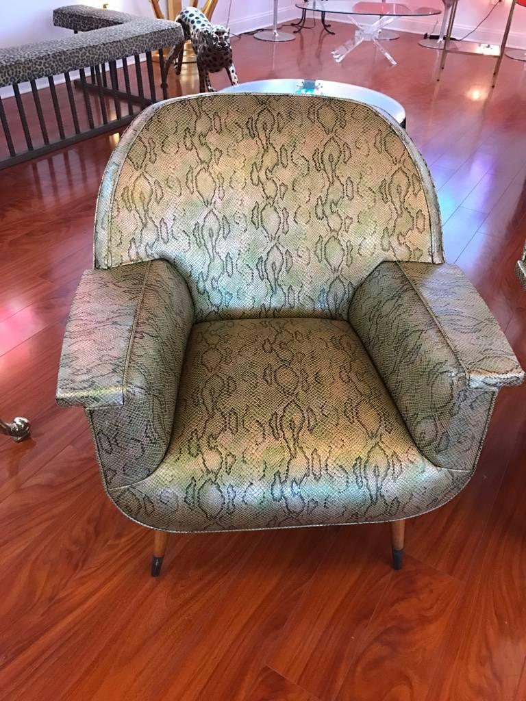 Stunning pair of Italian Mid-Century club chairs upholstered in faux snake skin. Having arched backs and flared arms, raised on turned and tapered legs.