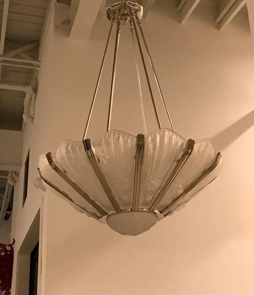 Stunning French Art Deco chandelier by the French artist Genet et Michon. Having twelve panels with a centre coupe in clear and frosted molded glass. With flower motif details mounted in polished nickel geometric bronze frame.