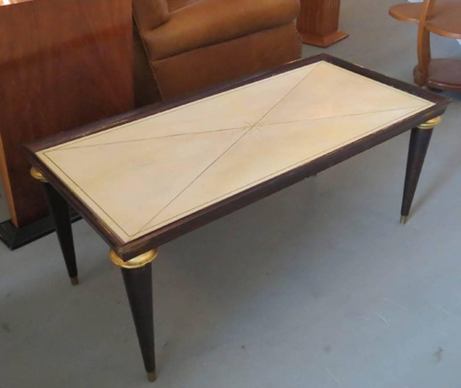 This French Art Deco coffee table is from Maison Jansen. The 1940s table is constructed of stained oak with gold leaf collars above the leg. The parchment table bed has a decorative 1940s design and feet are brass tipped the parchment has a glass
