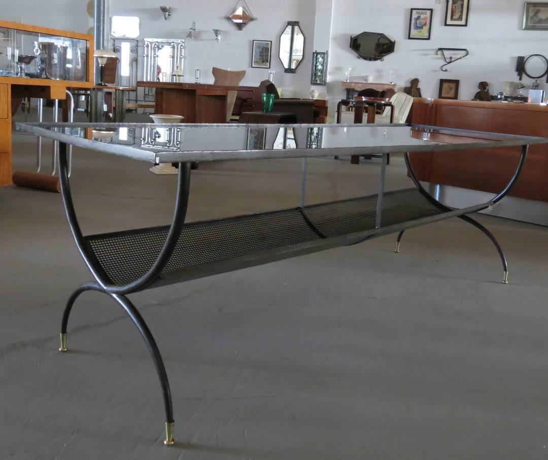 An exceptional French Art Deco coffee table from the 1940s. The almost six foot long coffee table has two “U” supports with brass feet and two vertical “U”s which support the tray, which holds a top of reverse painted black glass with gold trim.