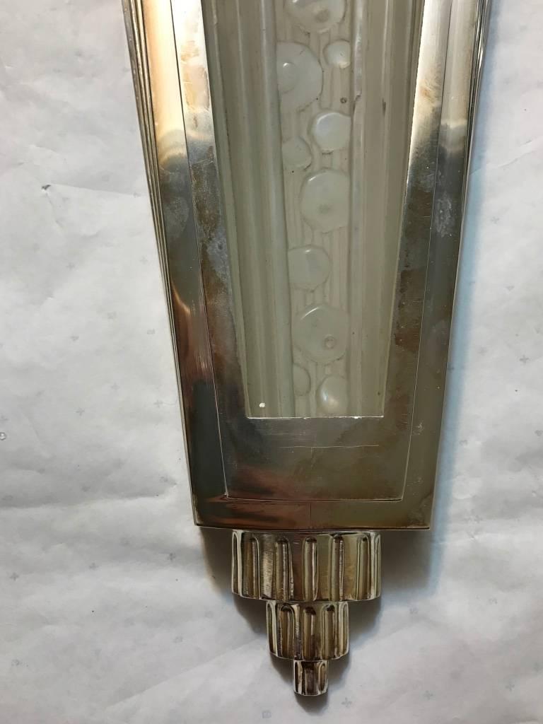 Pair of French Art Deco sconces. With clear frosted glass shades with intricate geometric motif details throughout. Each shade is held by a sterling silvered bronze multi-tiered skyscraper geometric design frame. Re plating upon request. 

  