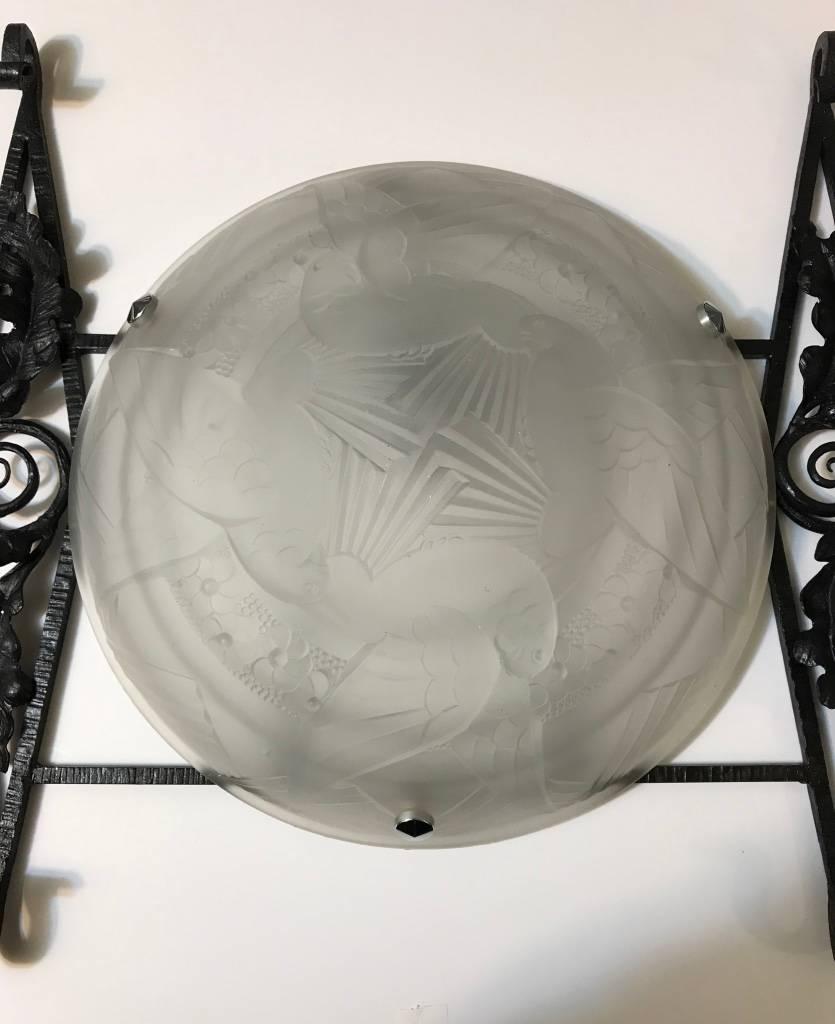 Splendida applique singola in stile Art Déco francese. Il paralume in vetro smerigliato trasparente presenta intricati dettagli geometrici e motivi di uccelli in volo. Il paralume è sostenuto da una cornice dal design geometrico e floreale. Re