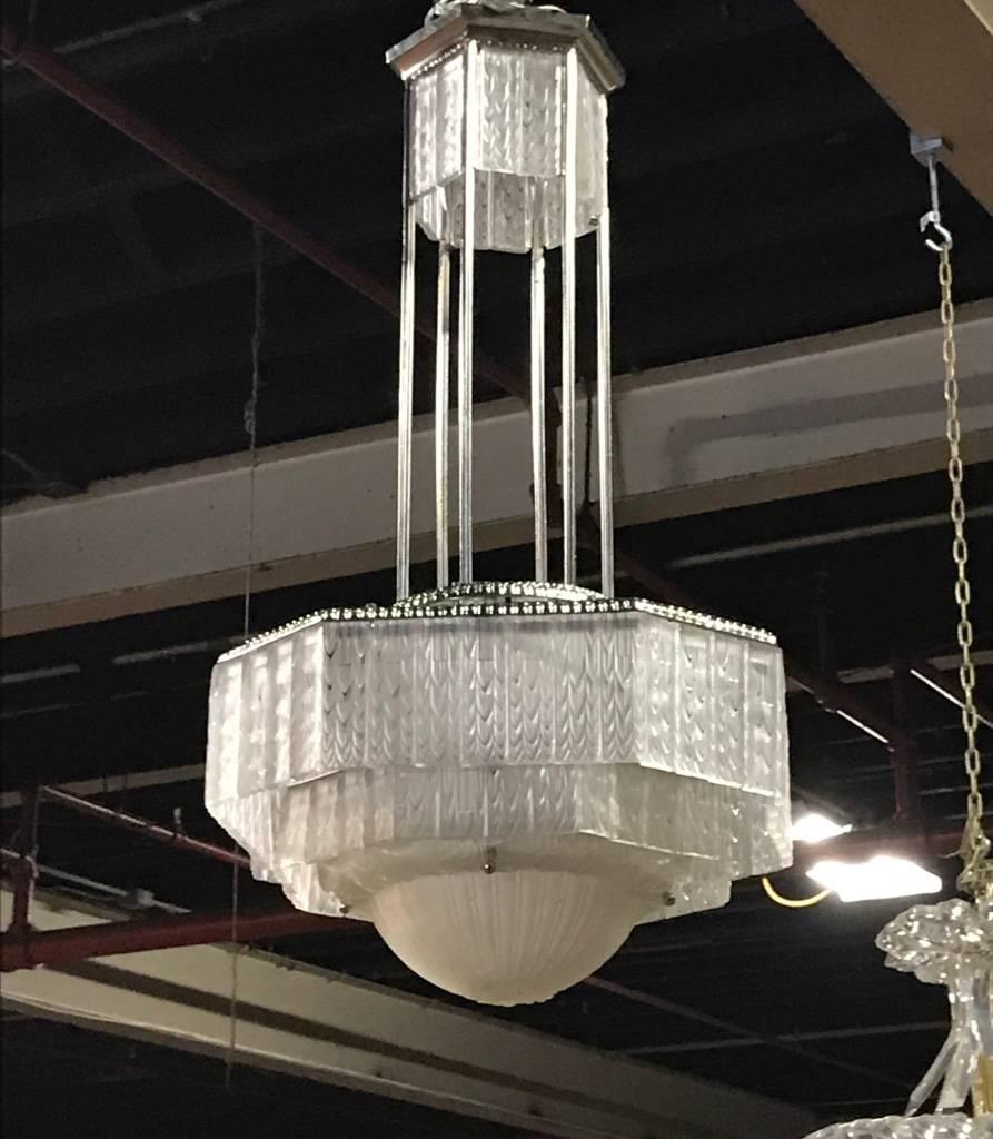 French Art Deco chandelier by French artist Georges Leleu. Having a clear frosted molded glass center coupe with geometric and ribbed motif. Surrounded by clear frosted molded glass panels with geometric motif. Mounted on a polished silver design