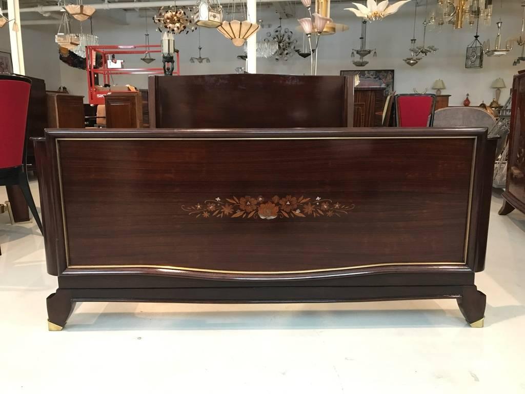 Stunning French Art Deco bed. Having beautiful mother-of-pearl inlay forming a floral motif with brass hardware, which accents the beauty of the wood. European full that can be turned into Queen bed. Matching nightstands and armoire that tie into