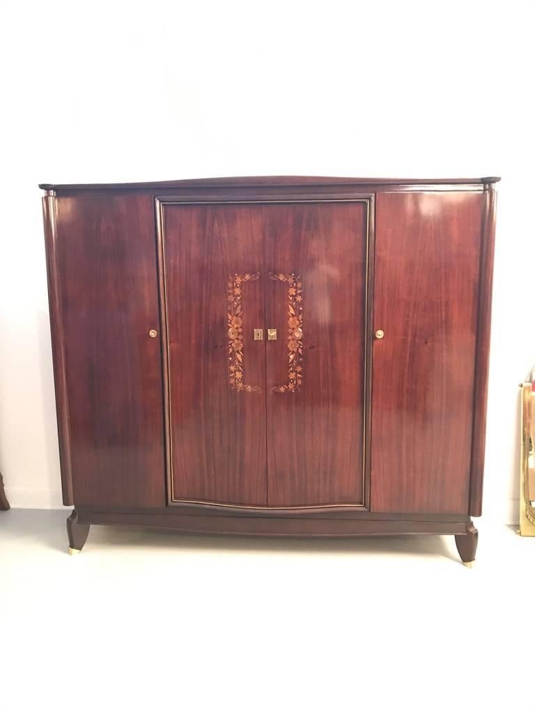Stunning French Art Deco Armoire. Having beautiful mother-of-pearl inlay forming a floral motif with brass hardware, which accents the beauty of the wood. Matching nightstands and bed that tie into the motif.