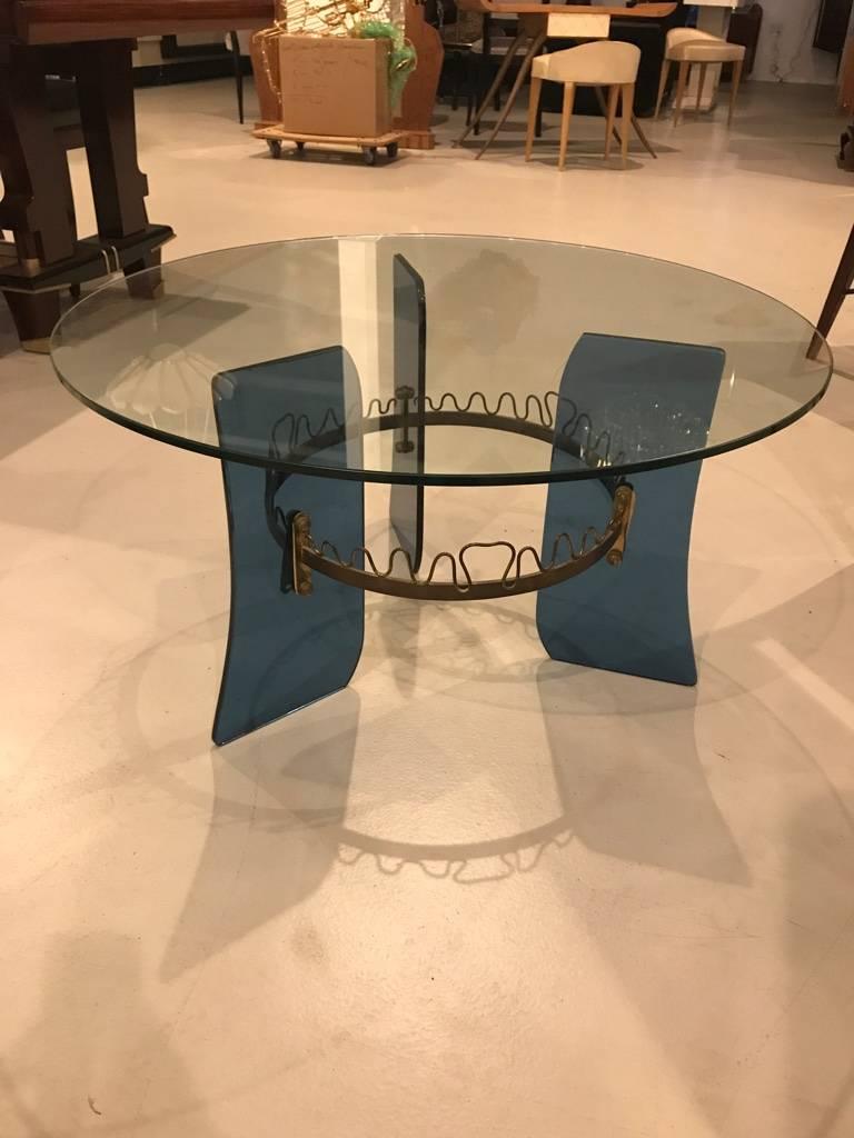 Italian Mid-Century Modern coffee table. Having circular clear glass top over three shaped supports in blue stained glass, connected with a stylized brass metal ring.