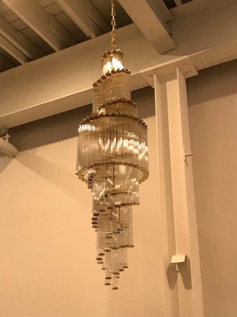 Mid-Century Modern Italian spiral chandelier. Having individual glass rods that form a circle with brass holders on the top and bottom that hang from hooks onto a spiral brass frame, as pictured. Any amount of chain can be added for custom hanging